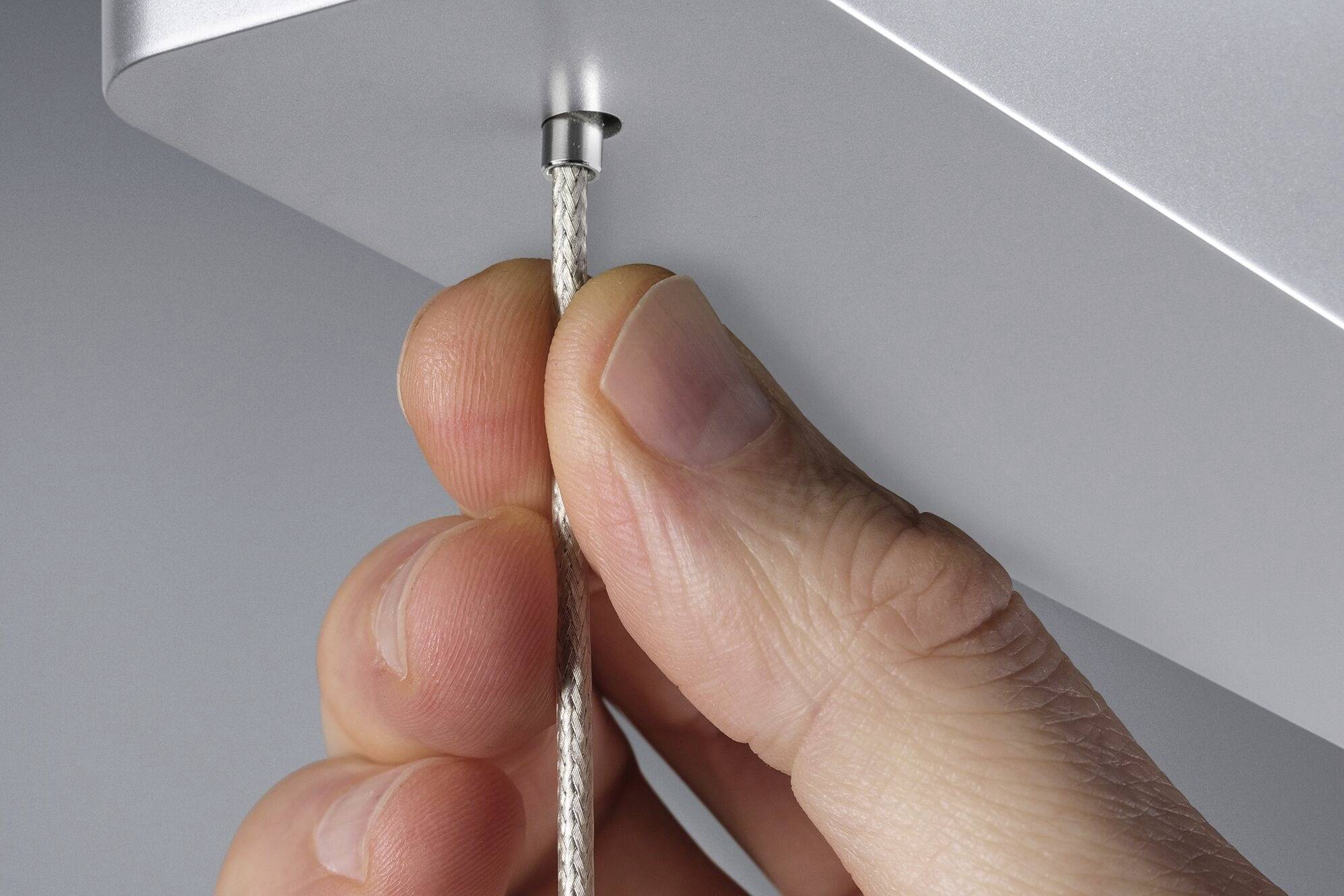 Ręka pociąga za cienką metalową linkę przywiązaną do srebrnej powierzchni.