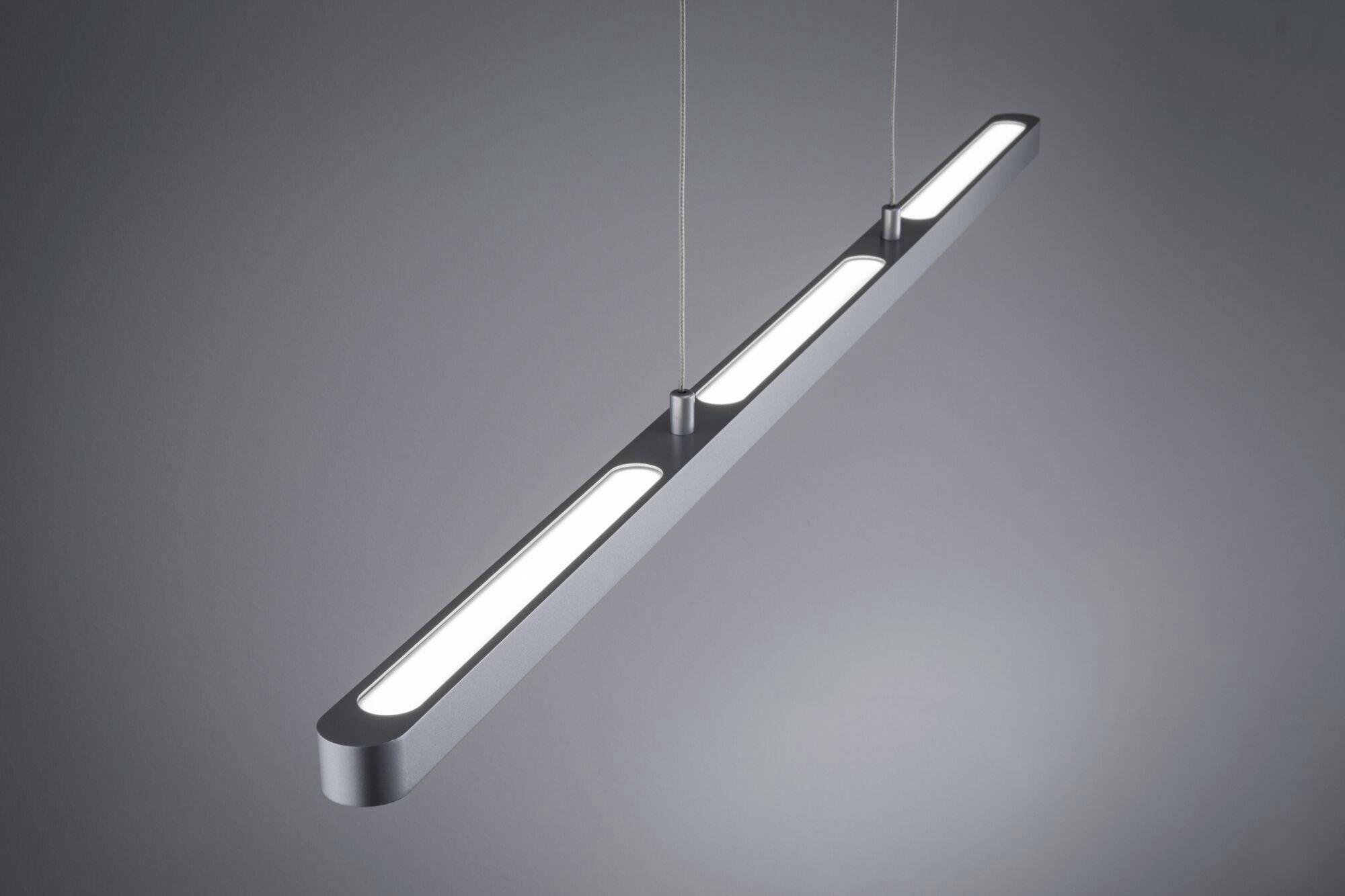 Nowoczesna, podłużna lampa wisząca z metalu z trzema powierzchniami świecącymi, zawieszona pod sufitem.