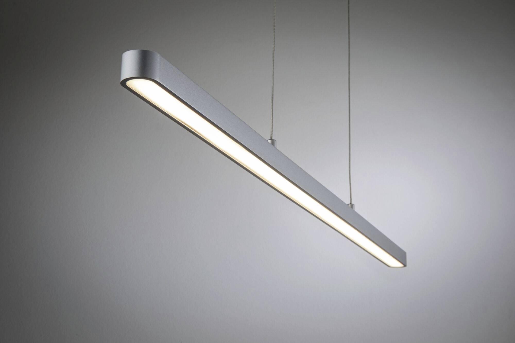 Nowoczesna, podłużna lampa sufitowa z metalu, zawieszona na dwóch cienkich linkach, rozpraszająca miękkie światło; projekt minimalistyczny.