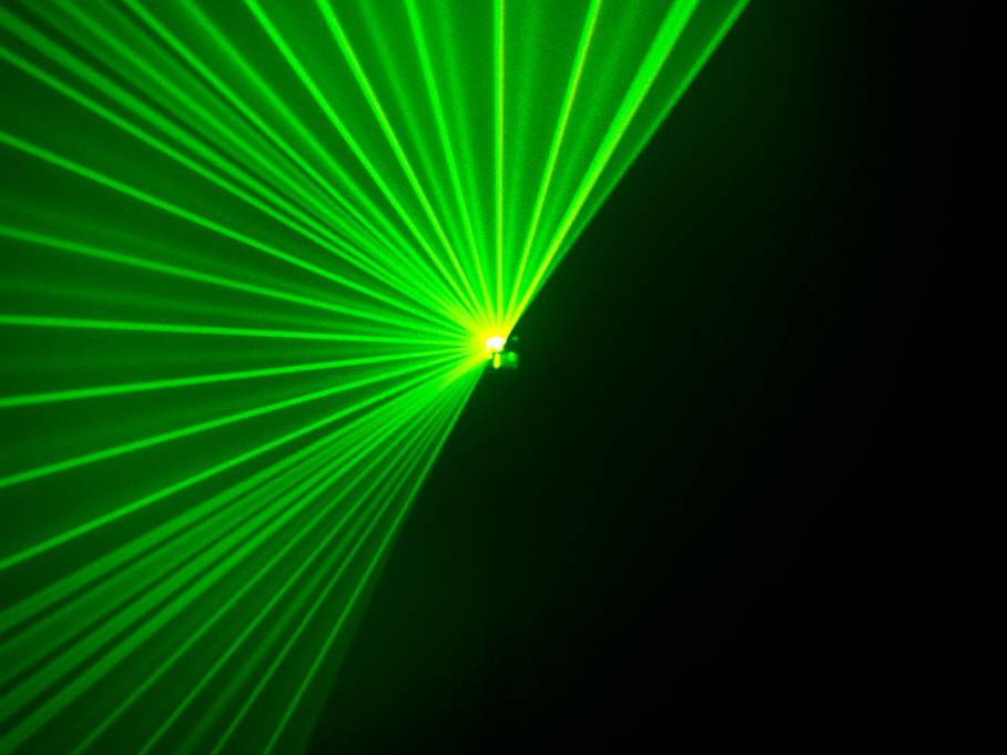 Zielone wiązki laserowe promieniują z centralnego punktu w różnych kierunkach, tworząc wizualny wzór w ciemności.
