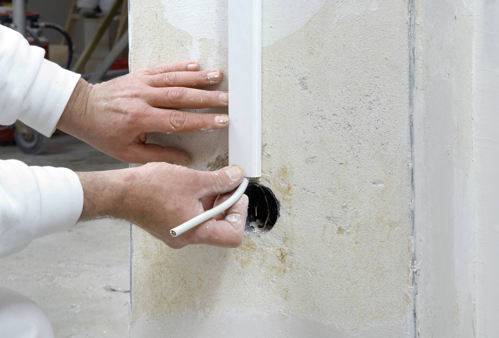 Osoba instaluje kabel w otworze ściennym, otoczona materiałami budowlanymi. Ręczne prowadzenie przewodów elektrycznych.