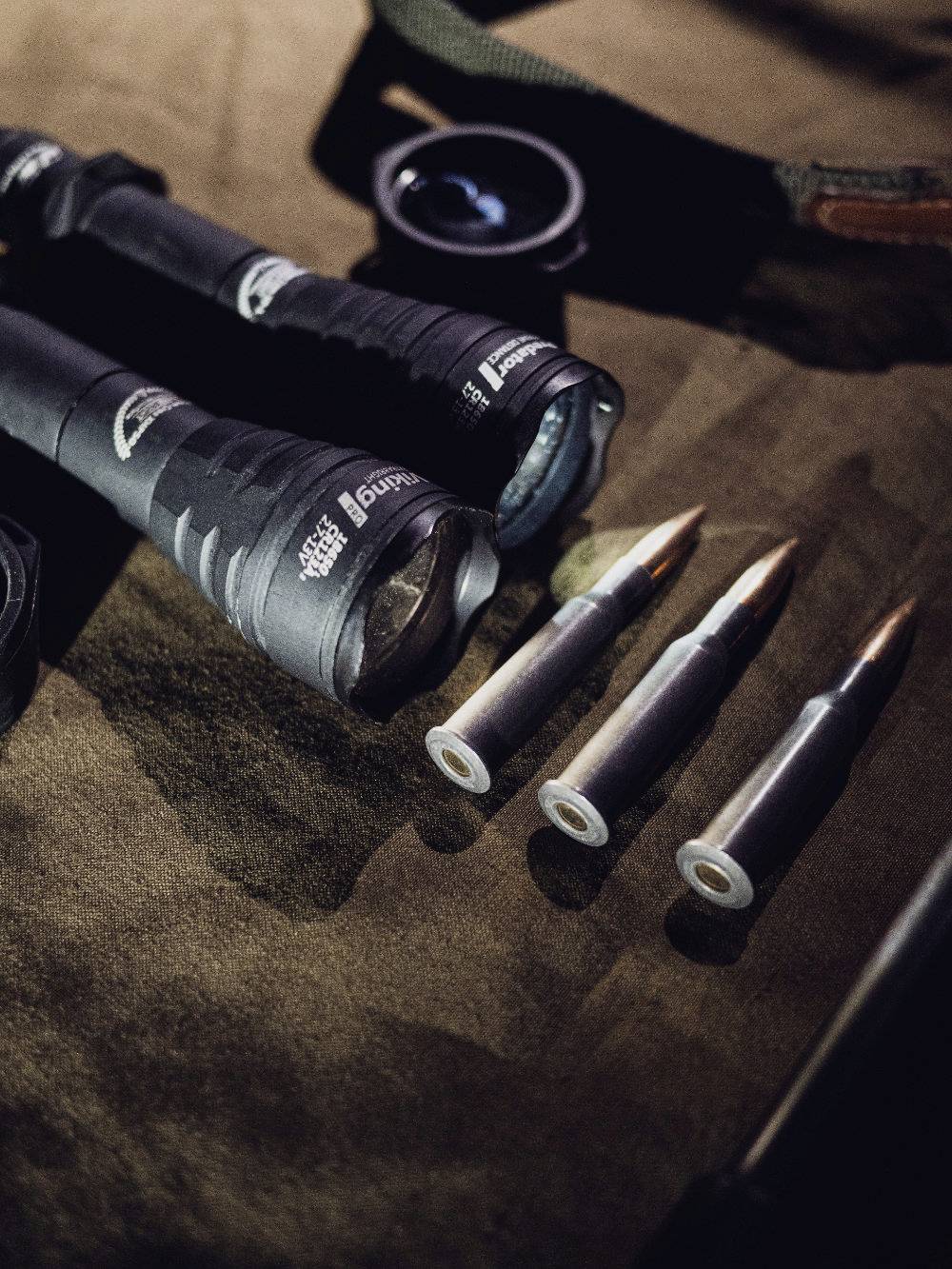 Na stole leżą latarki i trzy naboje, które ułożone są obok siebie w prostej linii.