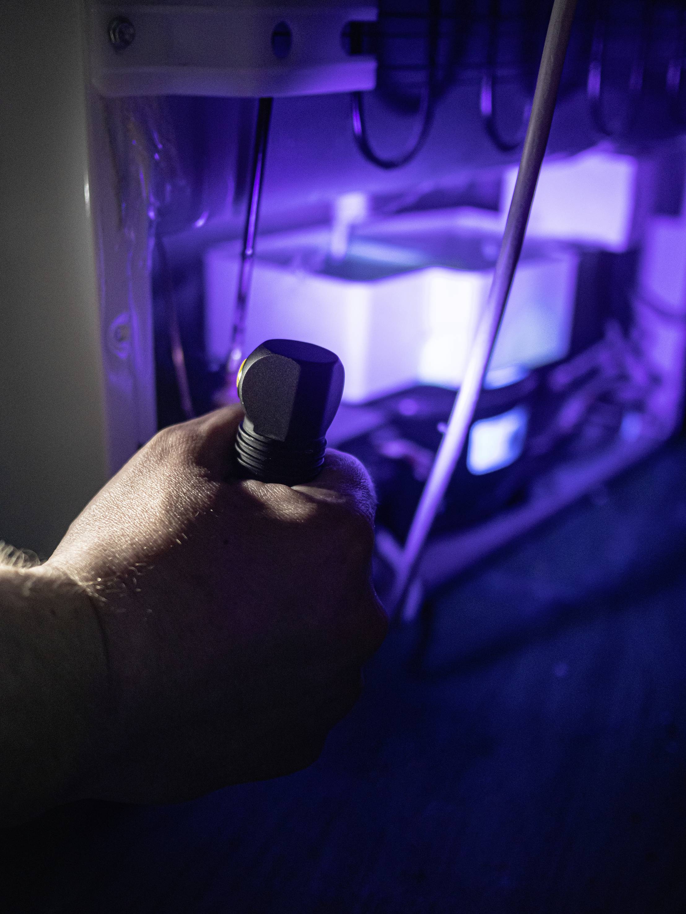 Ręka trzyma narzędzie skierowane na oświetlone komponenty lodówki, prawdopodobnie podczas naprawy.