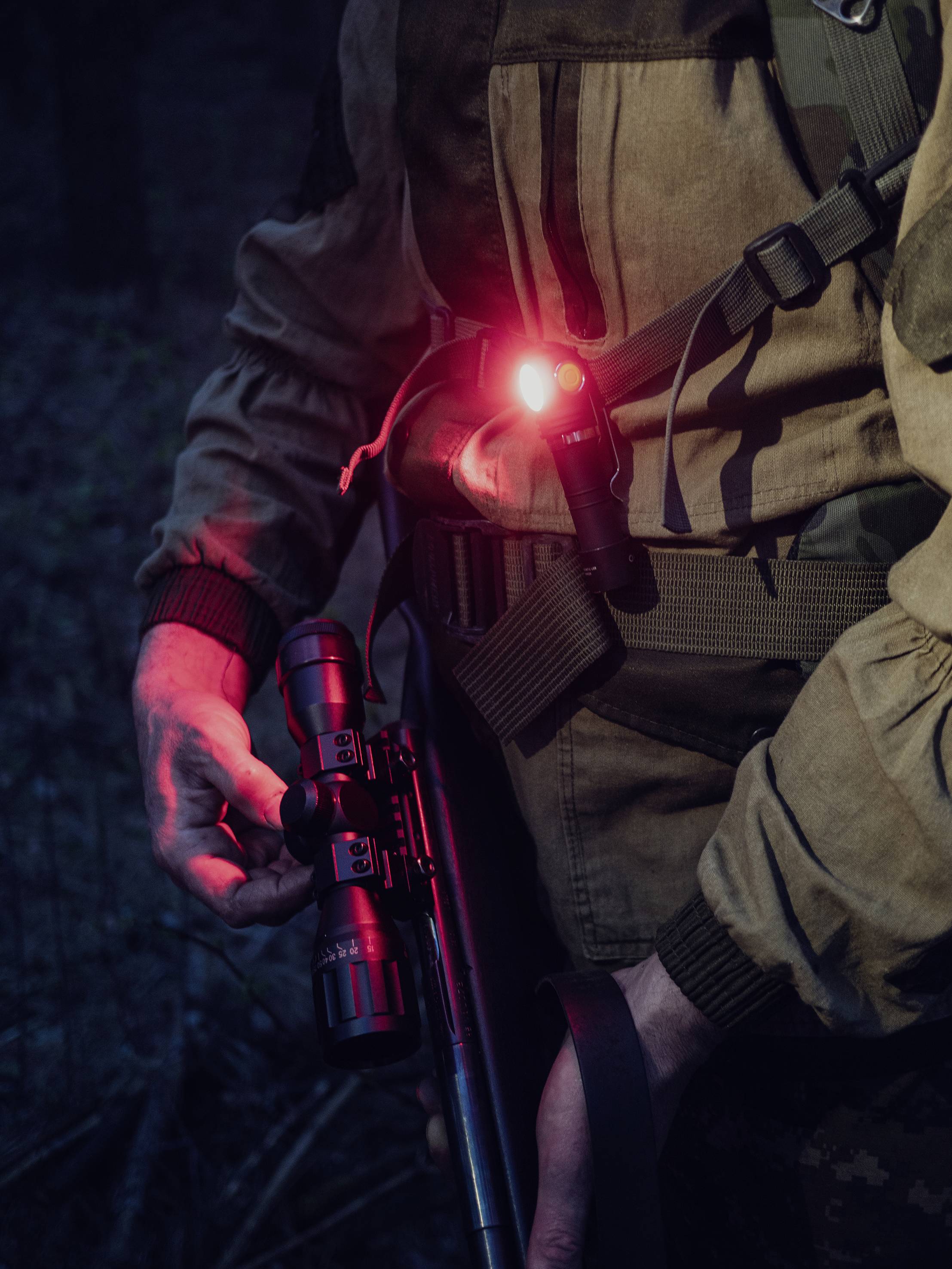 Osoba trzyma pistolet w prawej ręce i ma czerwoną latarkę przymocowaną do klatki piersiowej.