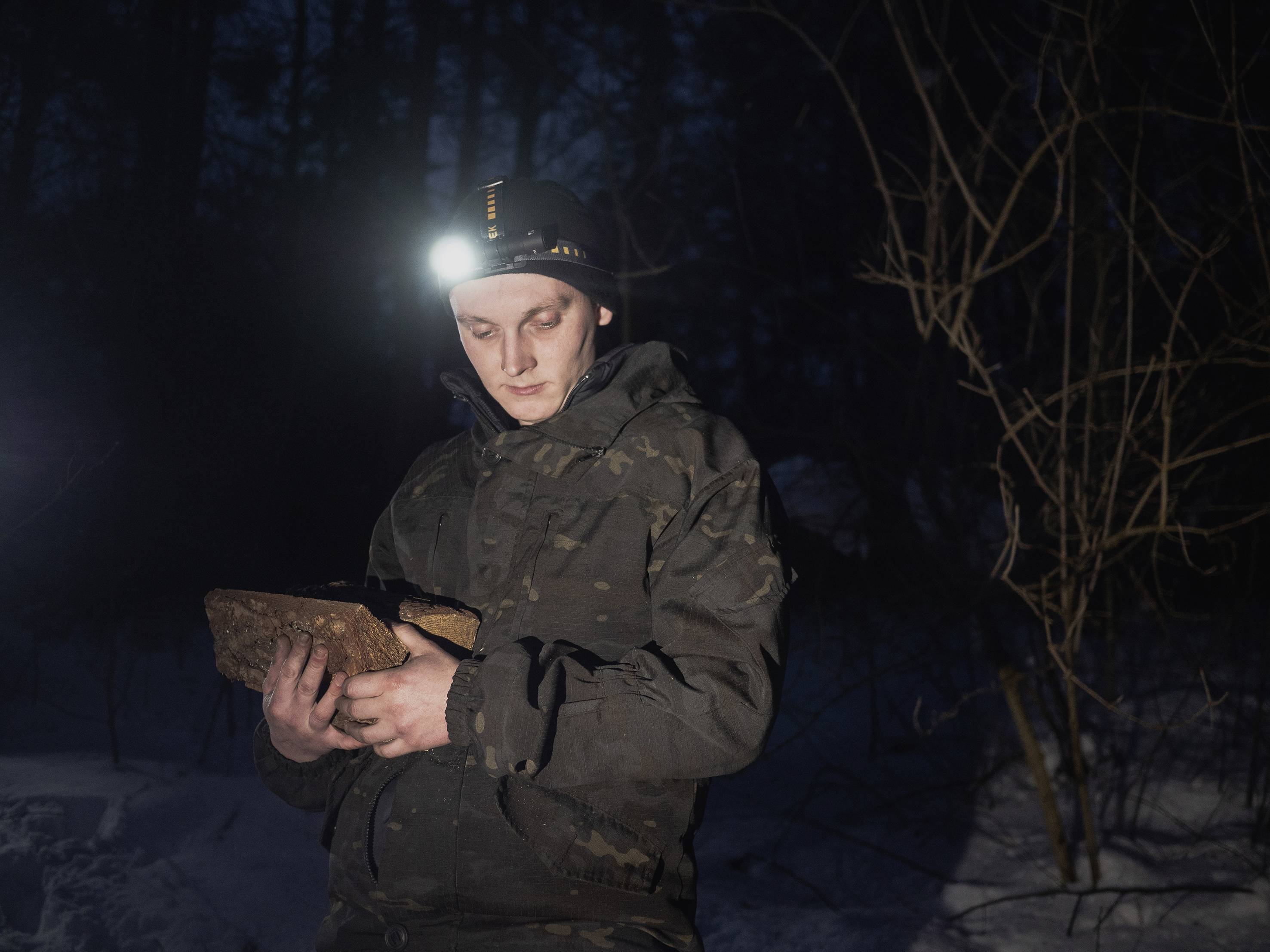 Osoba w kamuflażu stoi nocą w lesie i czyta książkę. Czołówka oświetla książkę, podczas gdy wokół panuje ciemność.