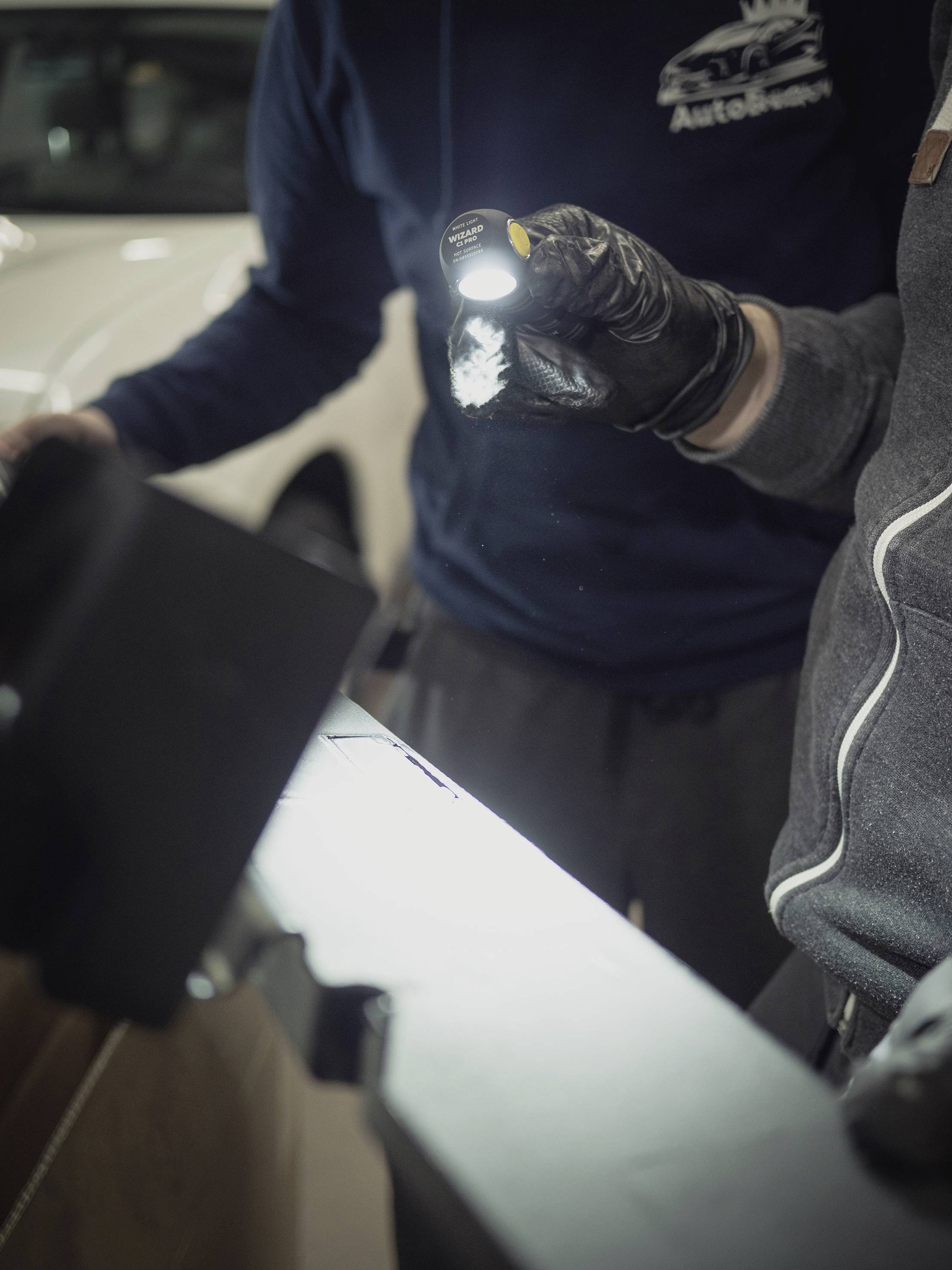 Dwie osoby kontrolują samochód latarką. Jedna osoba trzyma lampę, podczas gdy druga dokładnie bada pojazd.