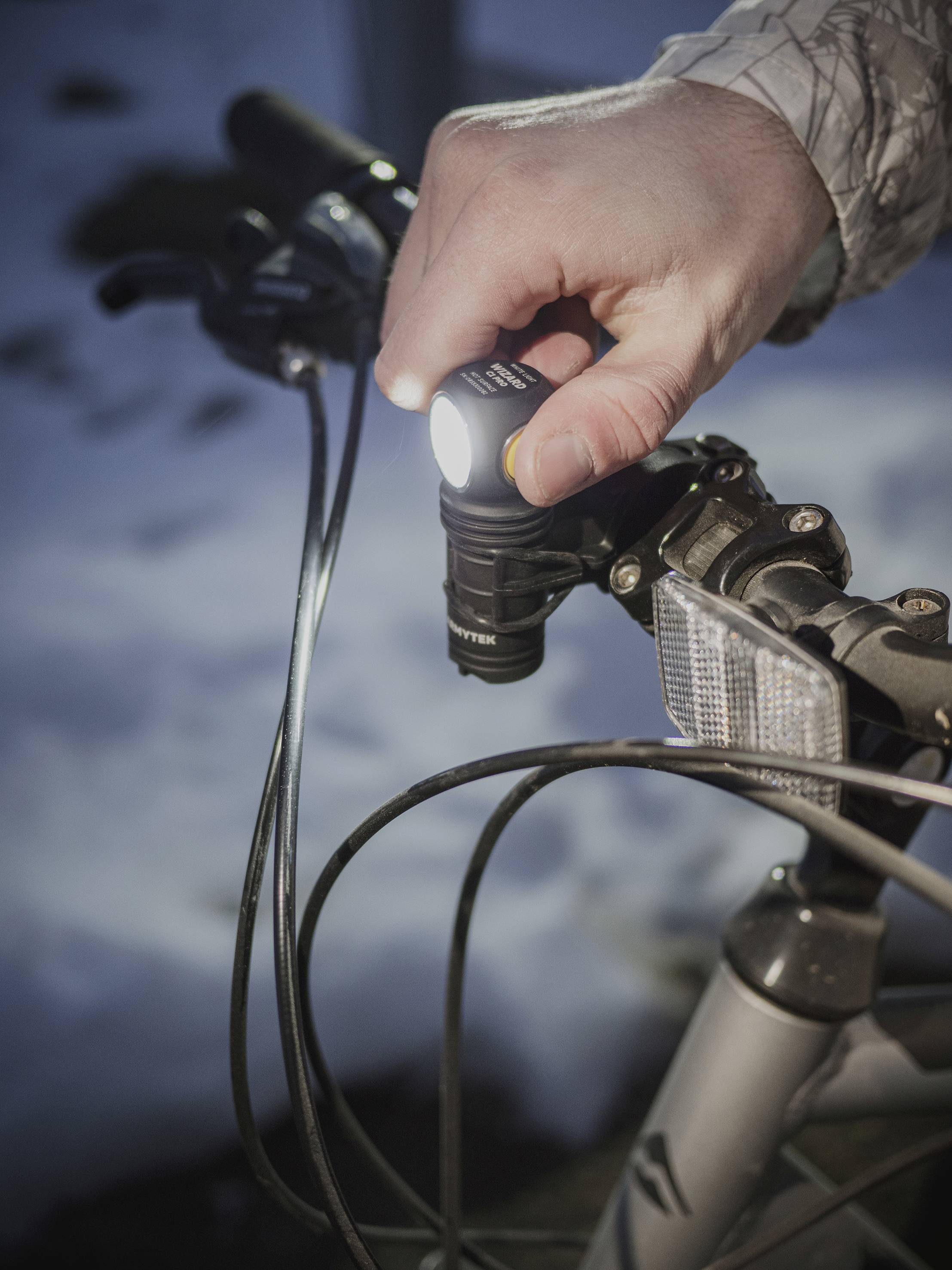 Ręka włącza światło roweru. W tle widać śnieg, co wskazuje na zimowe warunki.