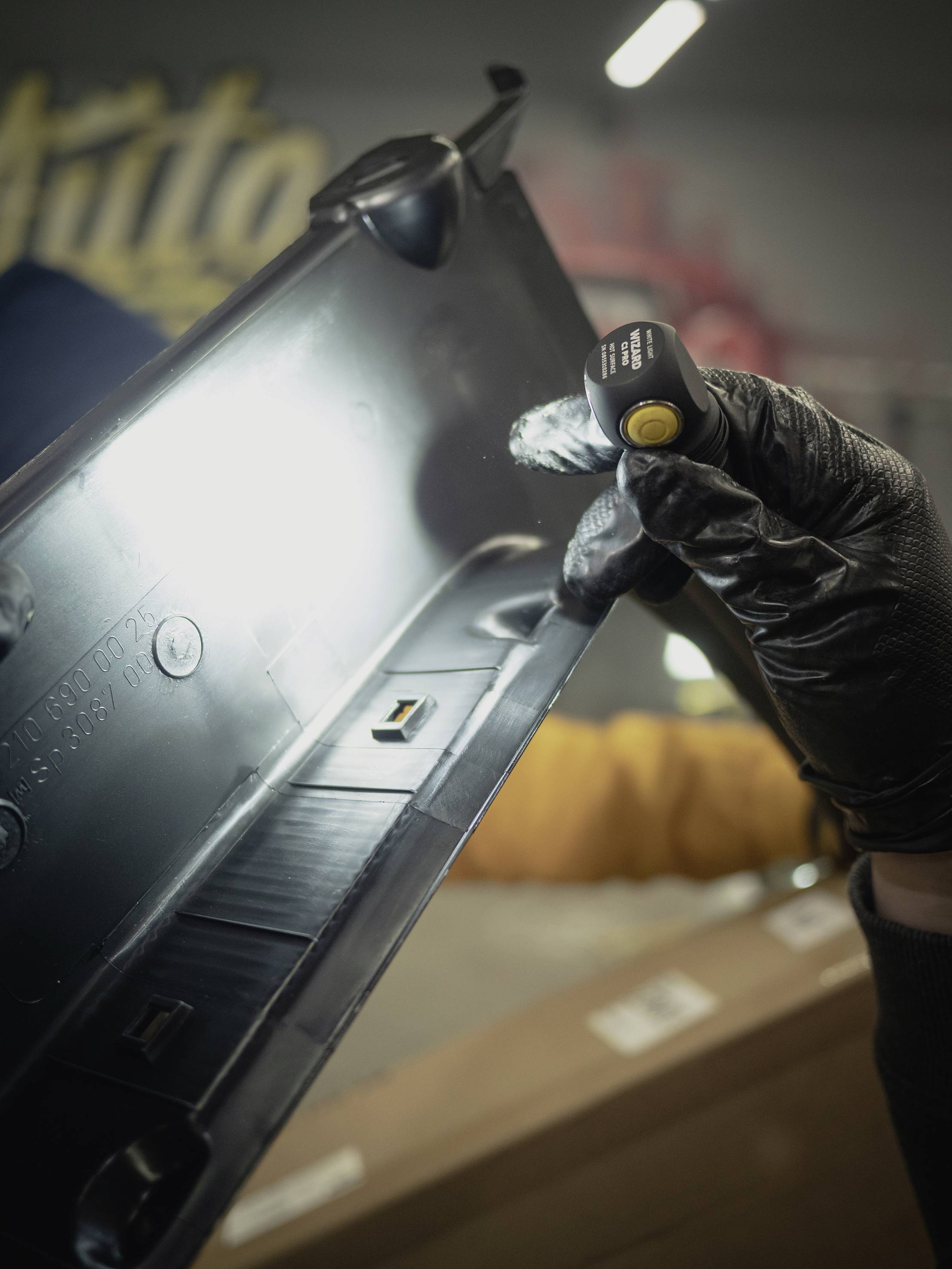 Osoba w czarnych rękawiczkach trzyma czarny element plastikowy pod światło, aby go dokładnie zbadać.