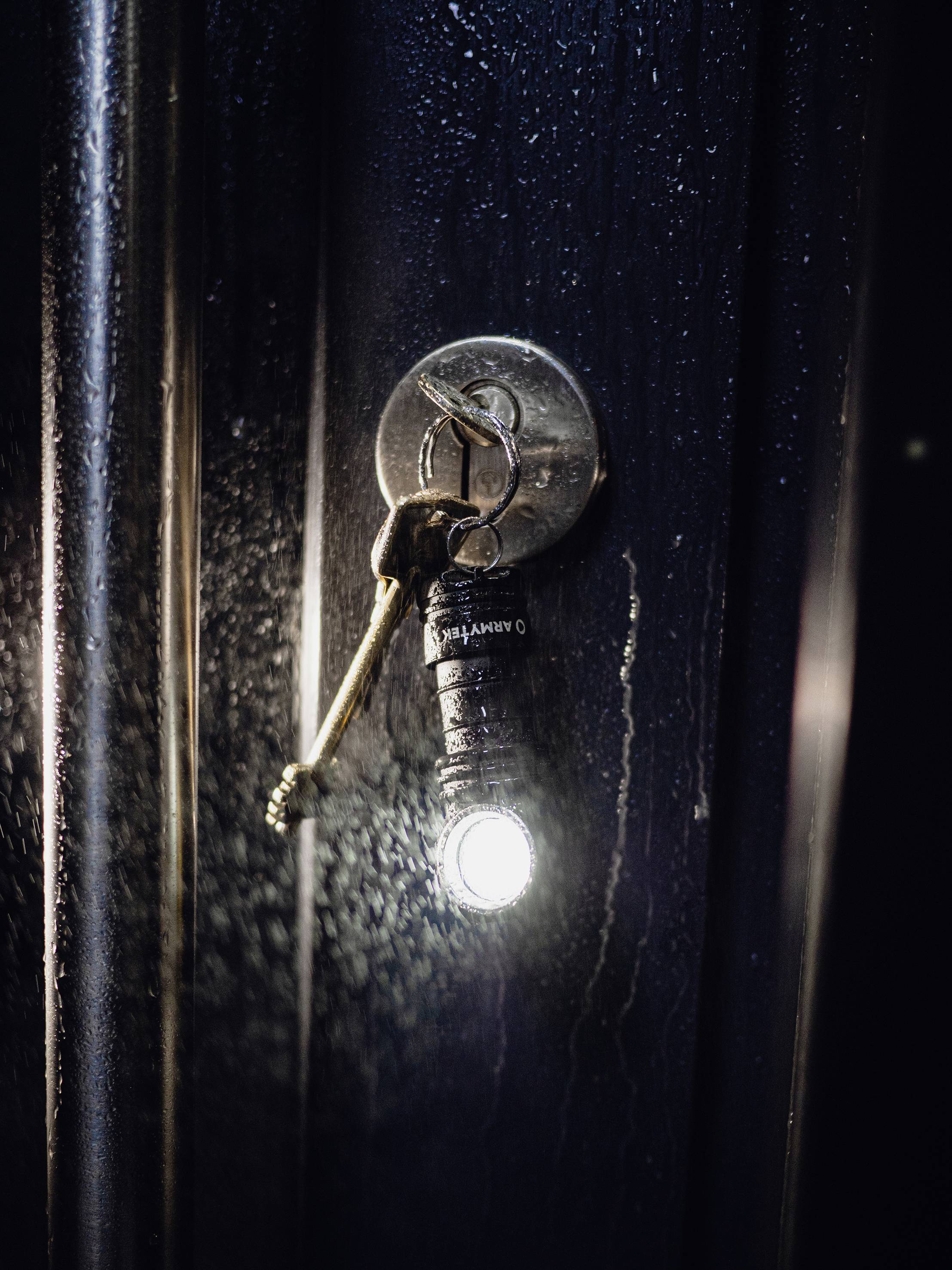 Klucz tkwi w zamku drzwiowym, do którego przymocowana jest świecąca mini latarka, oświetlająca ciemne drzwi.
