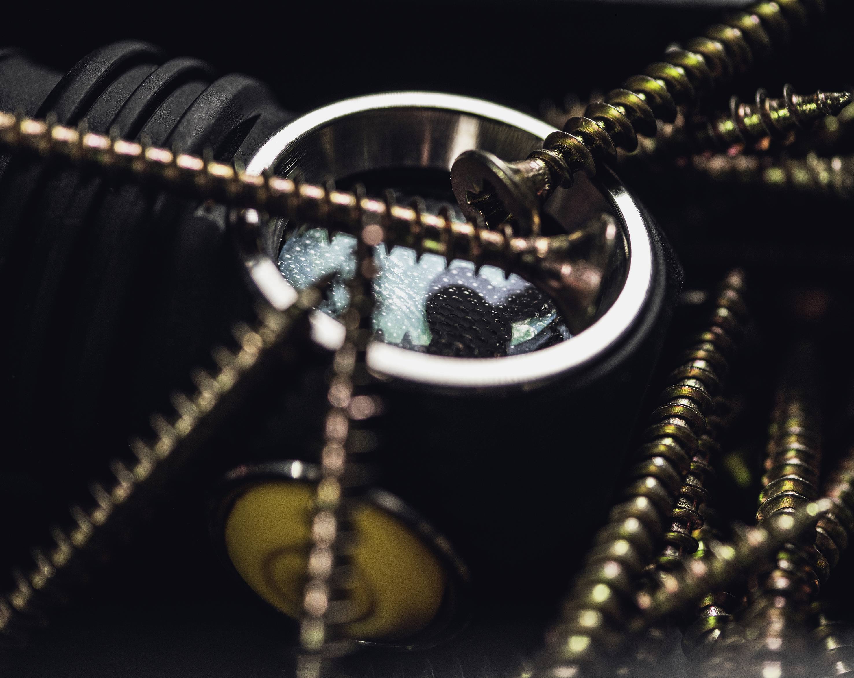 Zbliżenie metalowych elementów, w tym śrub i łożyska kulkowego. Scena jest ciemna, z naciskiem na faktury i połysk metali.