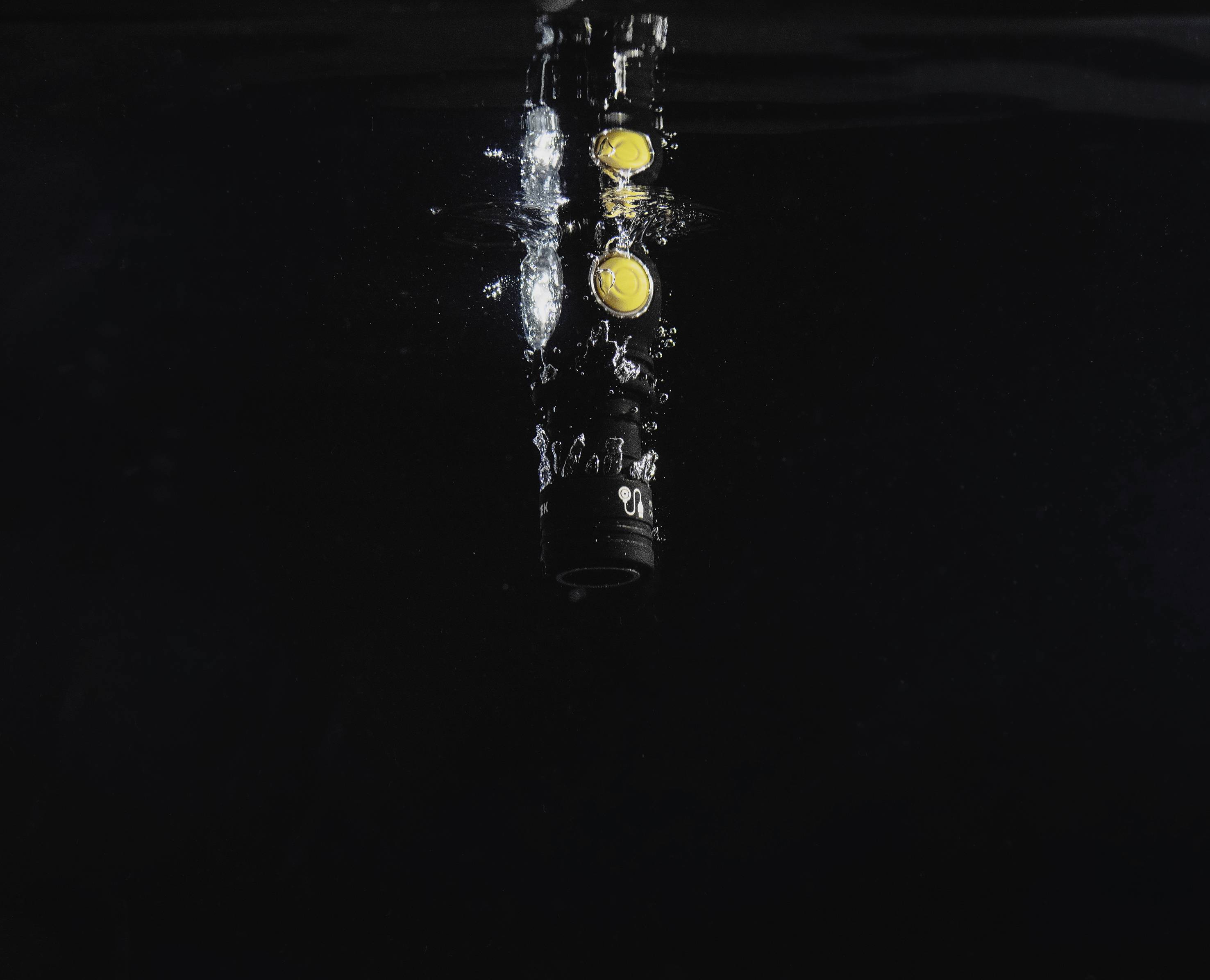 Latarka świeci pod wodą, pęcherzyki powietrza unoszą się w górę. Ciemne tło. Scena technologiczna przedstawiająca wodoszczelność.