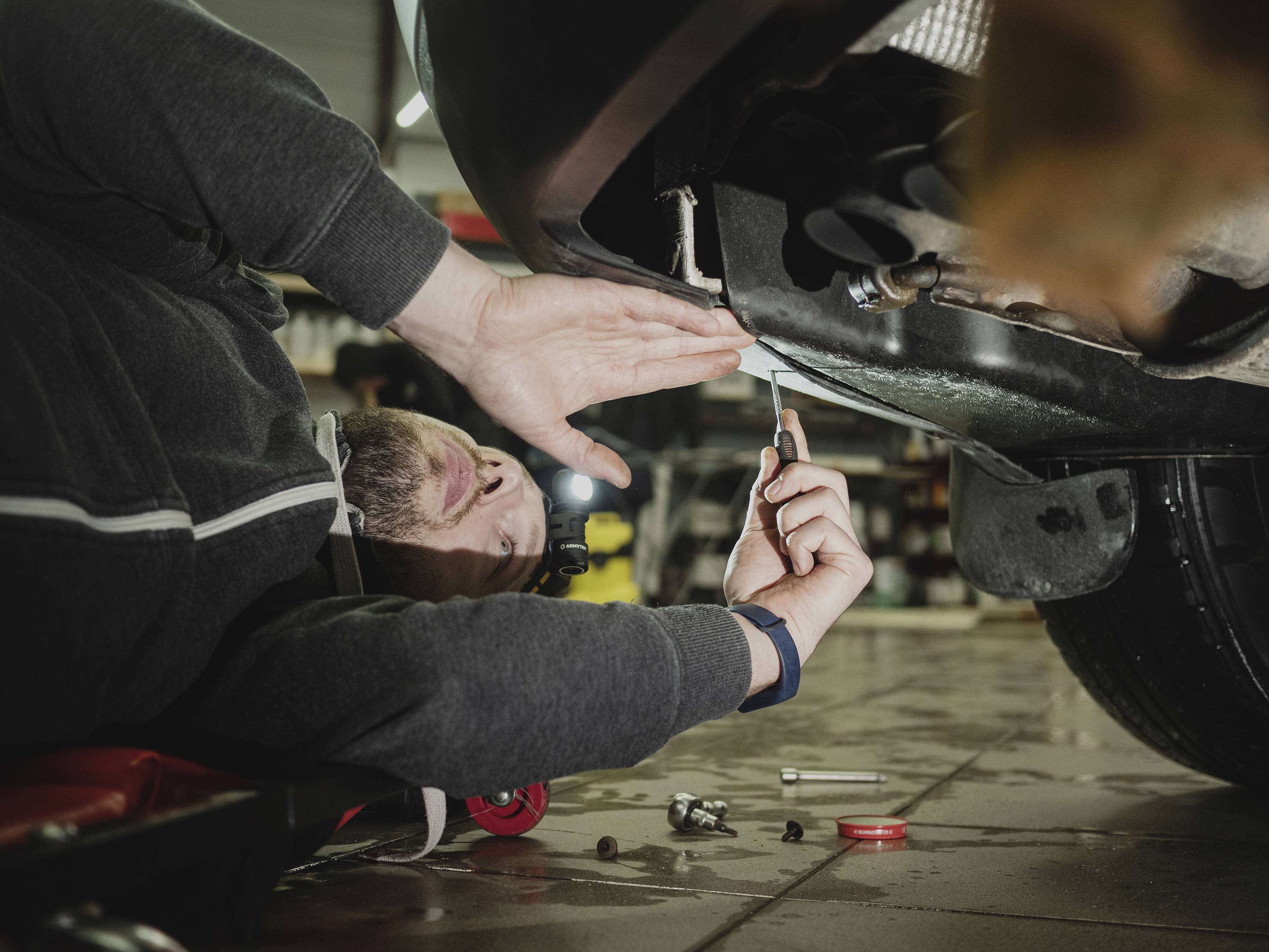Mechanik leży na plecach pod samochodem i pracuje kluczem przy dolnej części pojazdu.