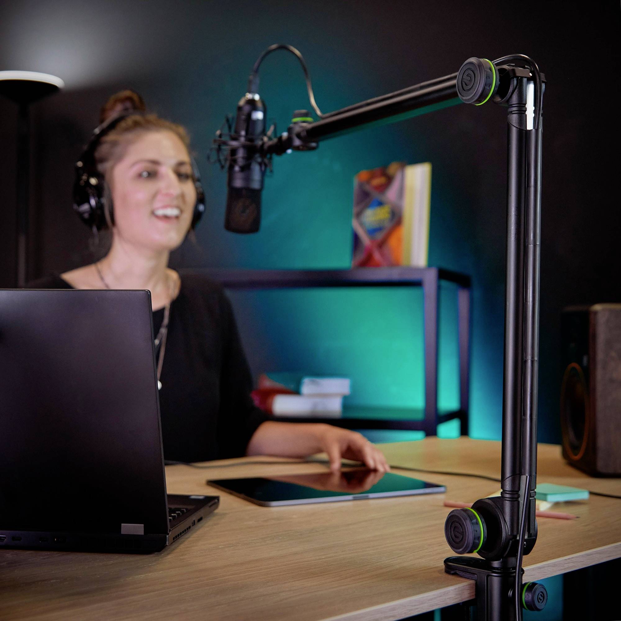 Podcaster siedzi przy biurku z mikrofonem i laptopem, nosi słuchawki, otoczony sprzętem technicznym.