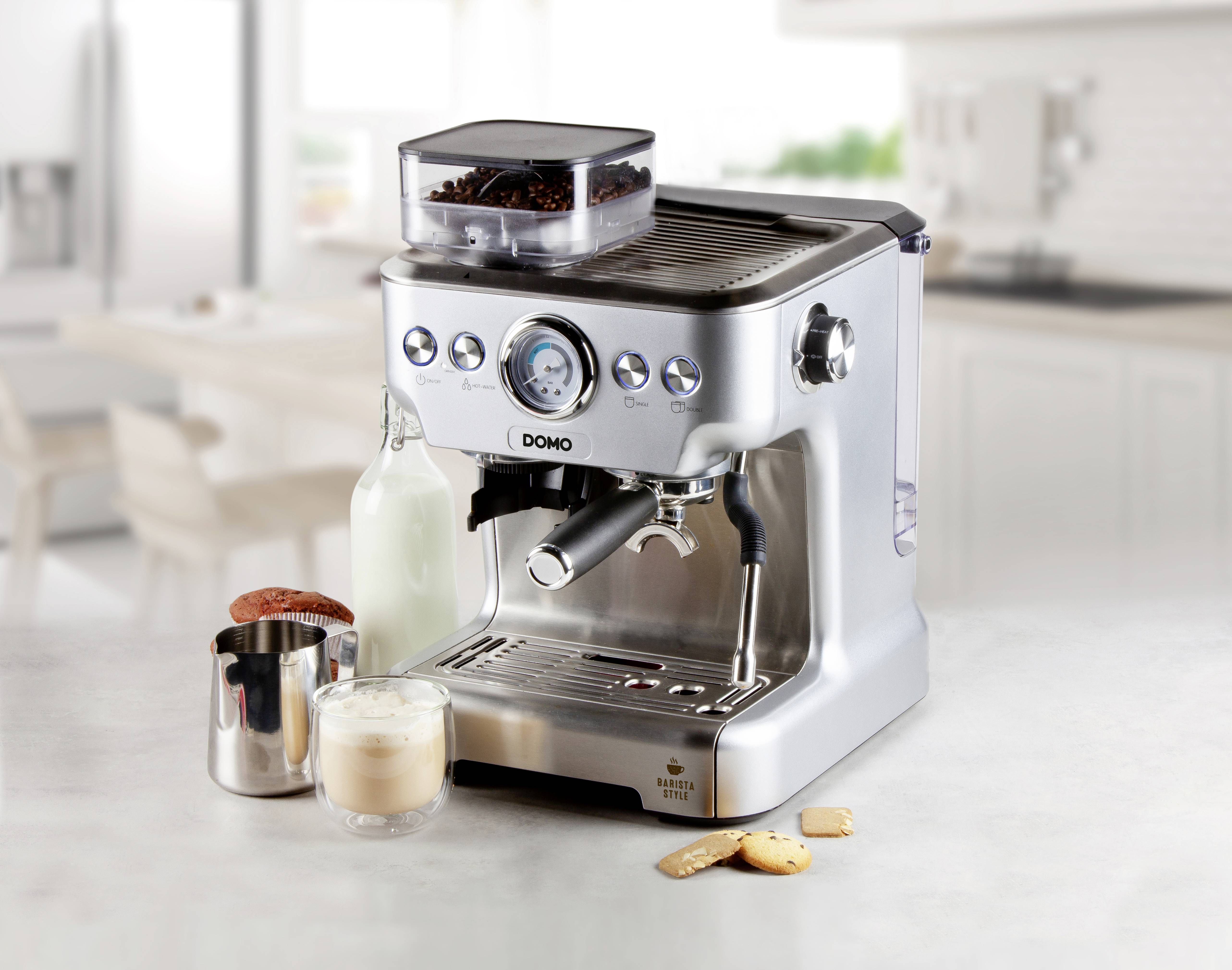 Srebrny ekspres do espresso na blacie kuchennym, otoczony dzbanuszkiem do mleka, szklanką mlecznej piany i ciasteczkami.