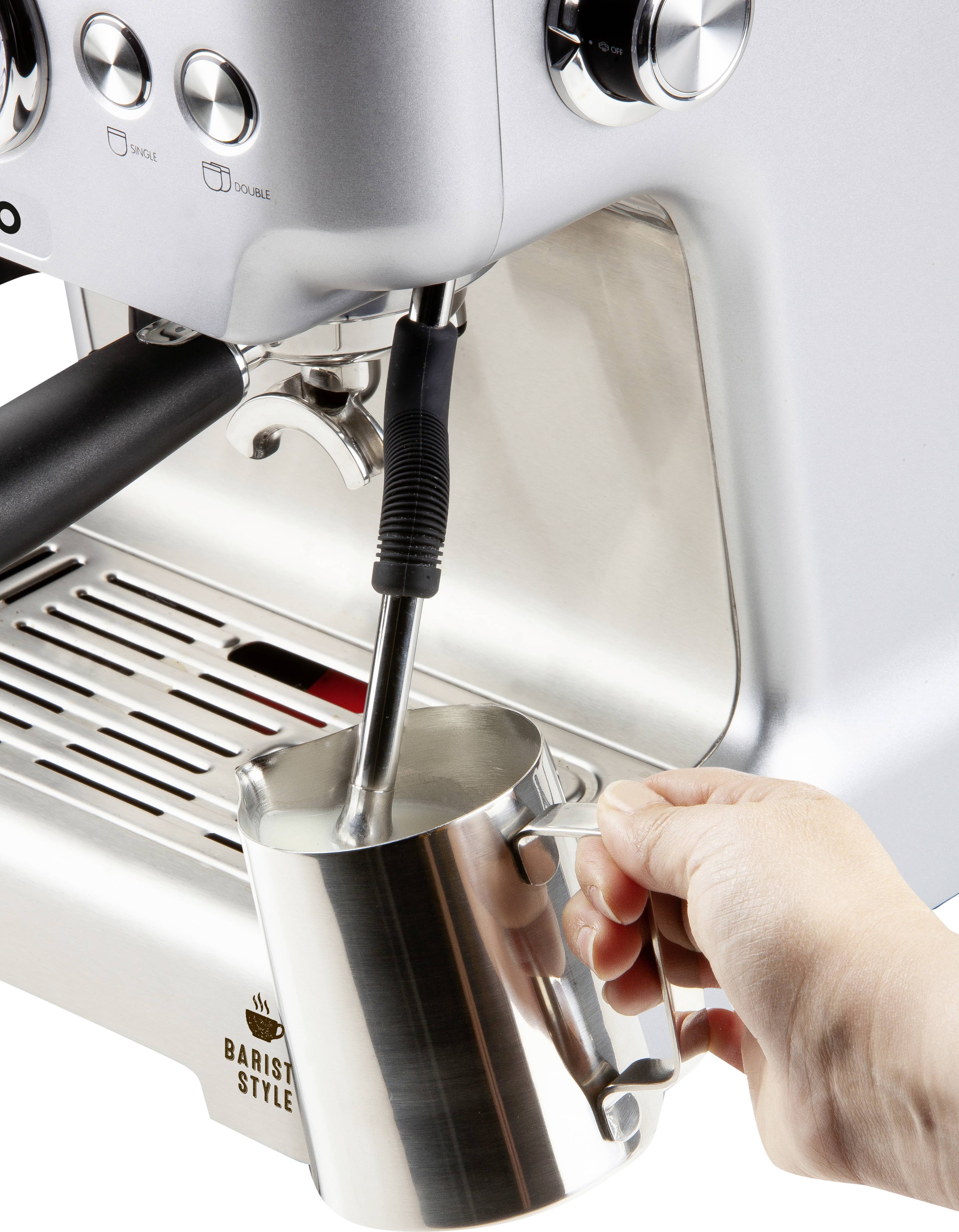 Ręka trzyma dzbanek na mleko pod dyszą parową ekspresu do kawy, aby spienić mleko.