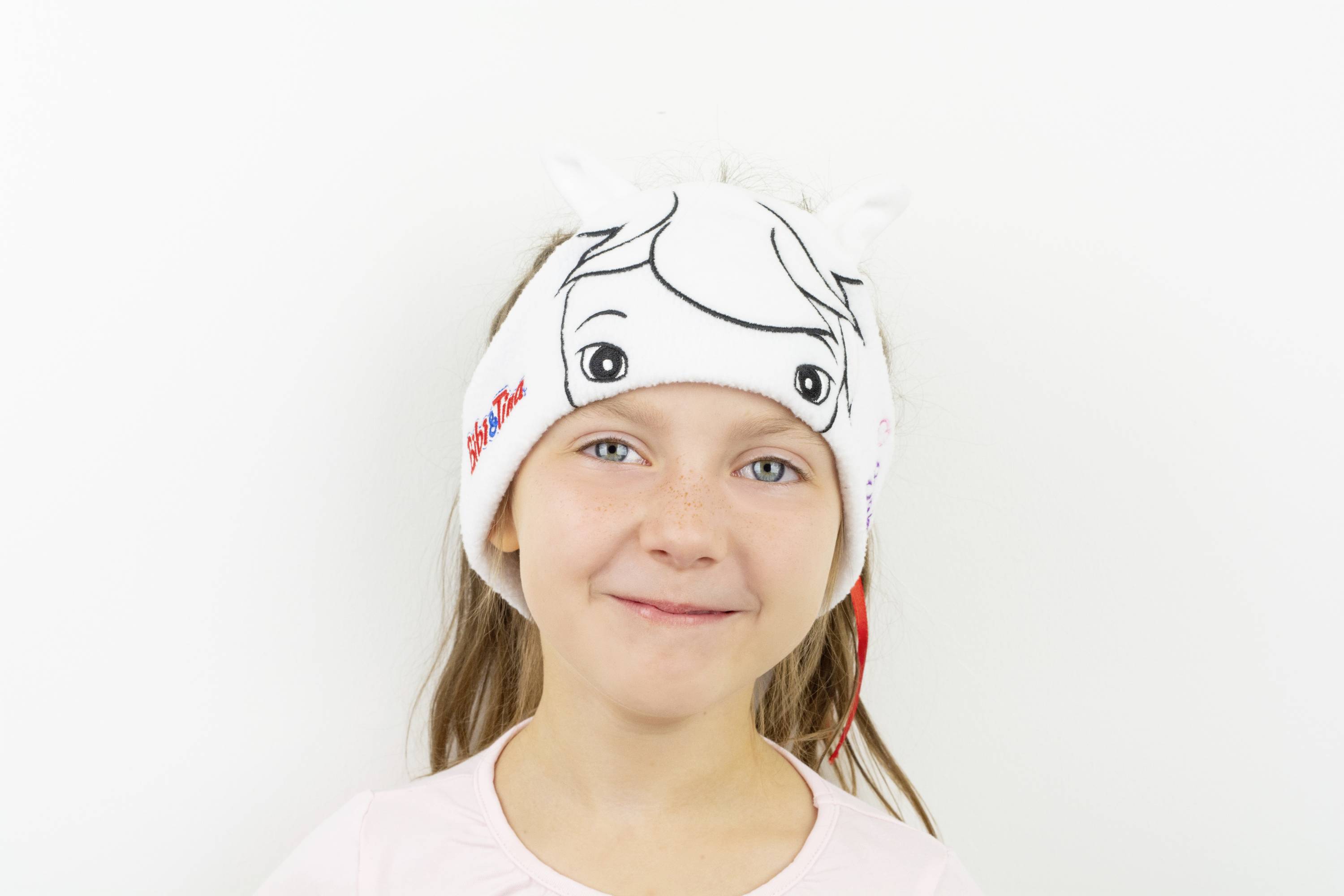 Dziewczynka uśmiecha się z białą opaską na głowie.