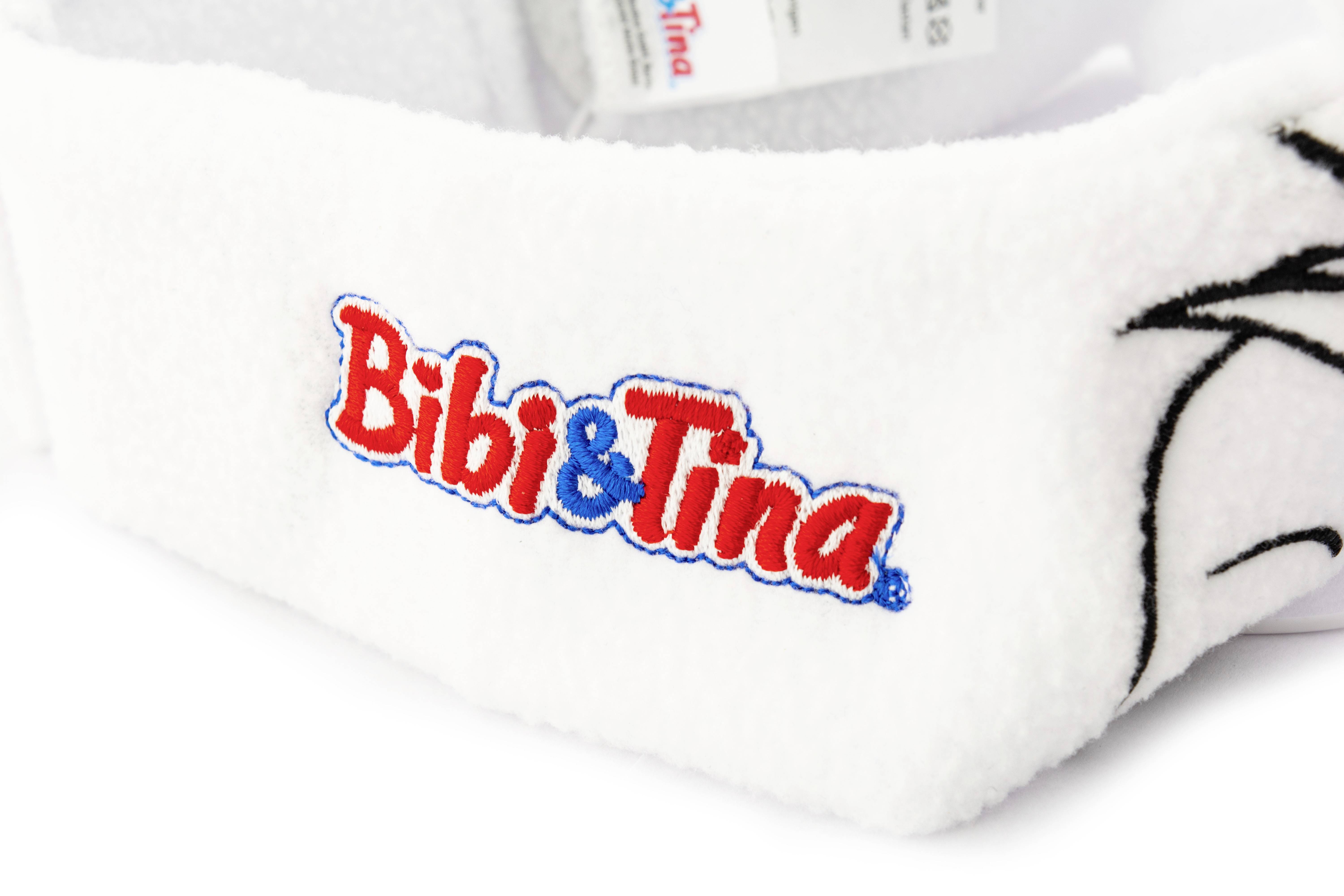 Biała opaska na głowę z wyhaftowanym logo 'Bibi & Tina' w kolorach czerwonym i niebieskim.