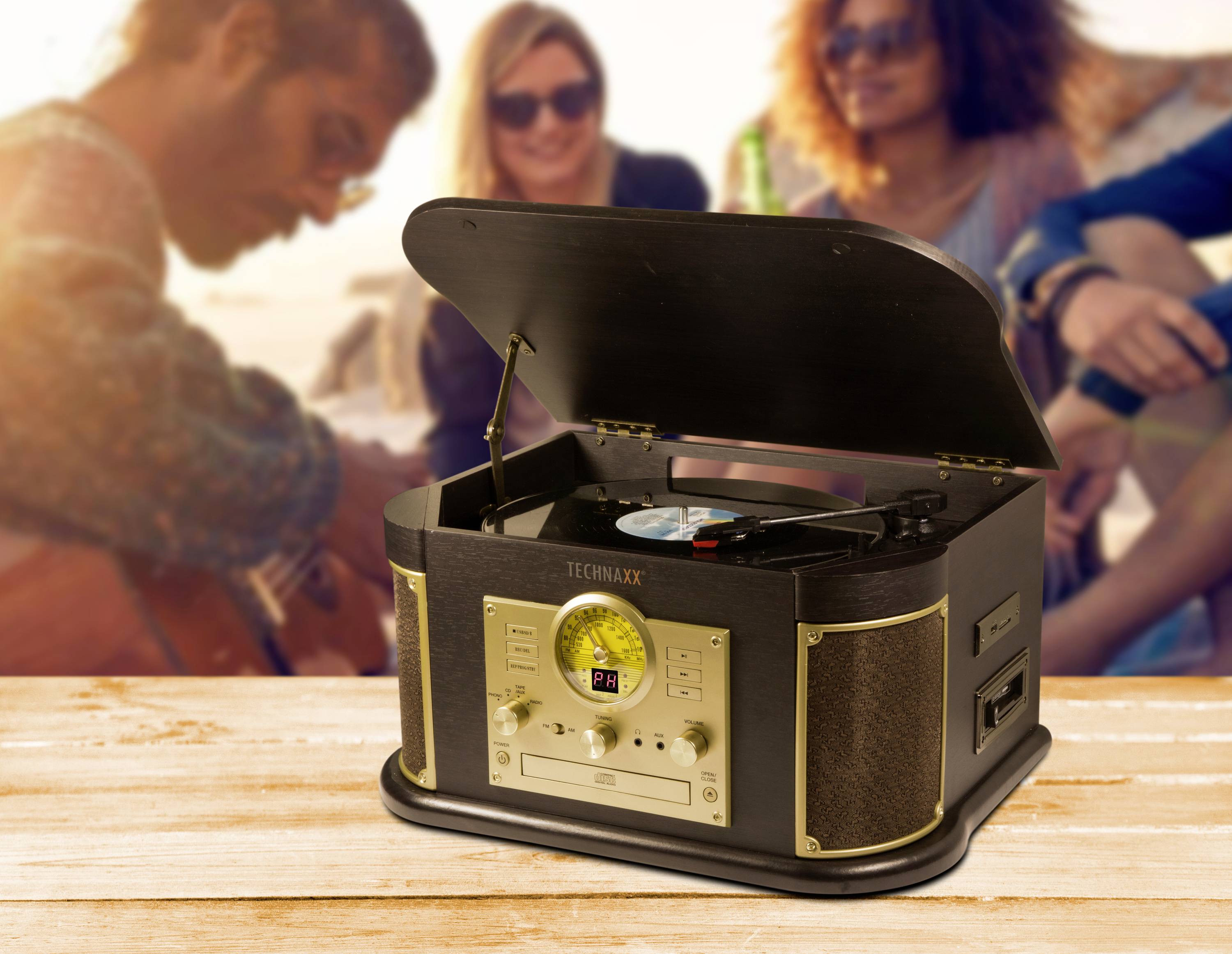 Zabytkowy gramofon w stylu vintage na drewnianym stole, otwarty z płytą winylową. W rozmytym tle ludzie nad plażą.