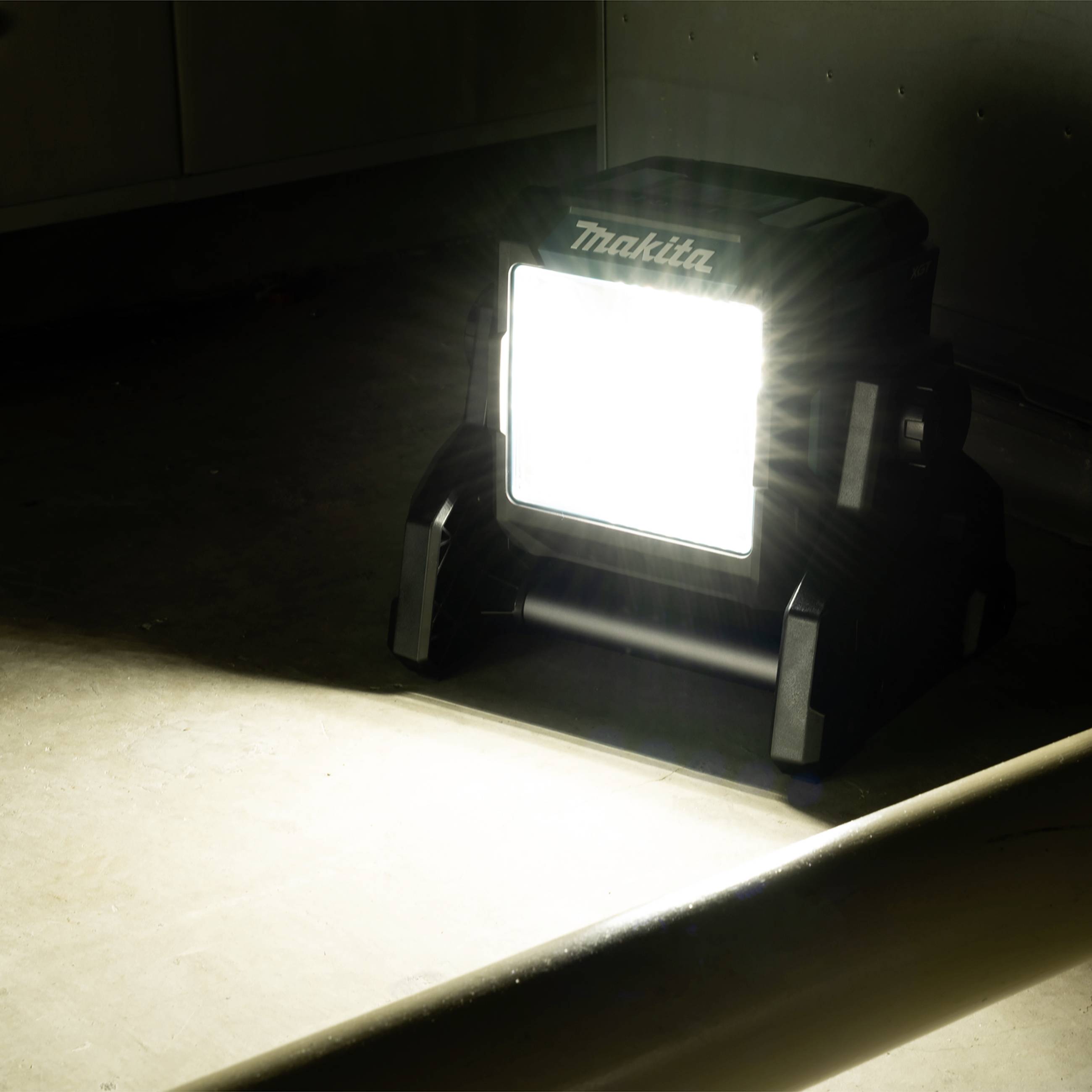 Jasna lampa budowlana oświetla pomieszczenie, podkreślając zapylone podłogę i ścianę.