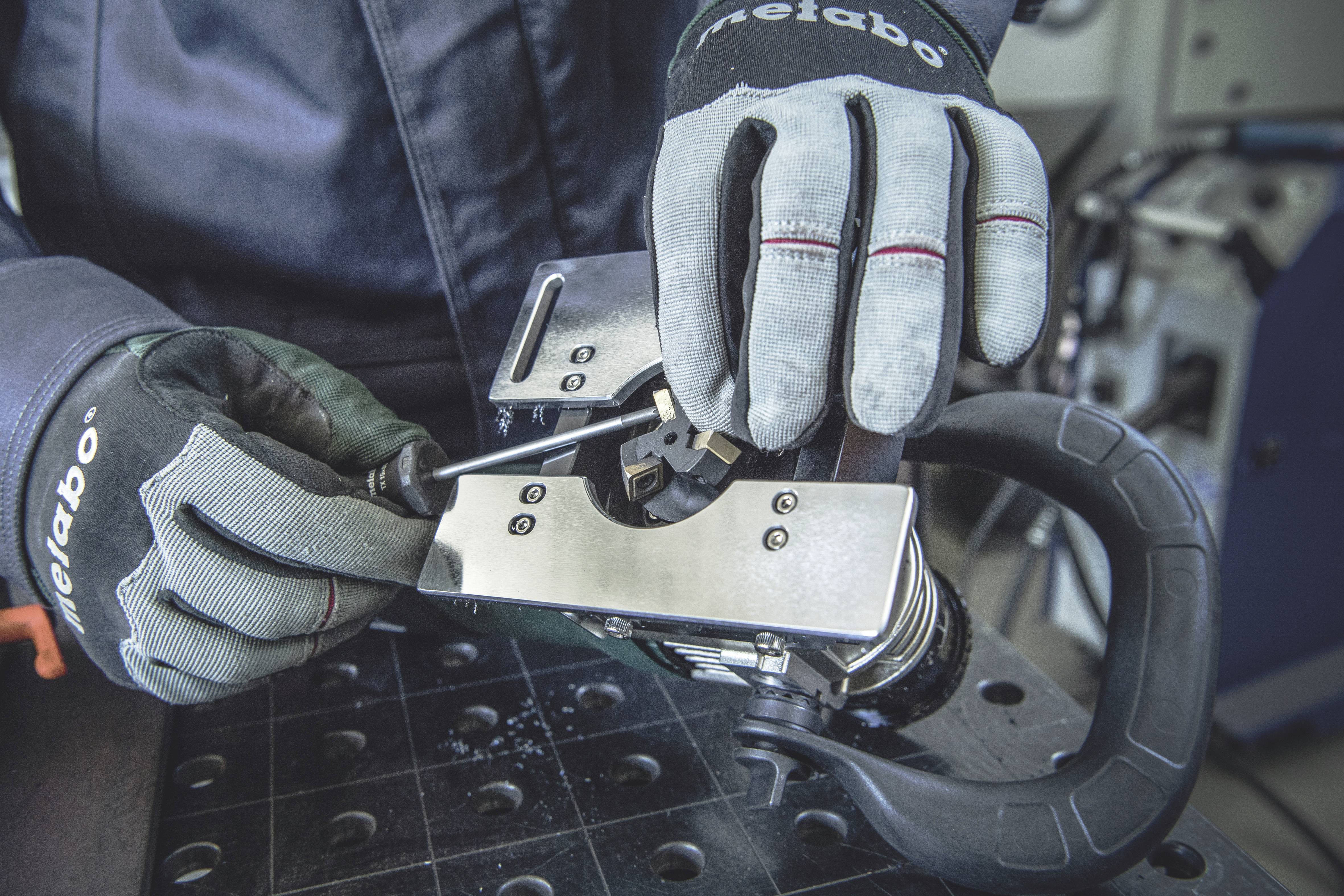 Osoba w rękawicach roboczych używa śrubokręta do regulacji metalowej maszyny na stole warsztatowym.