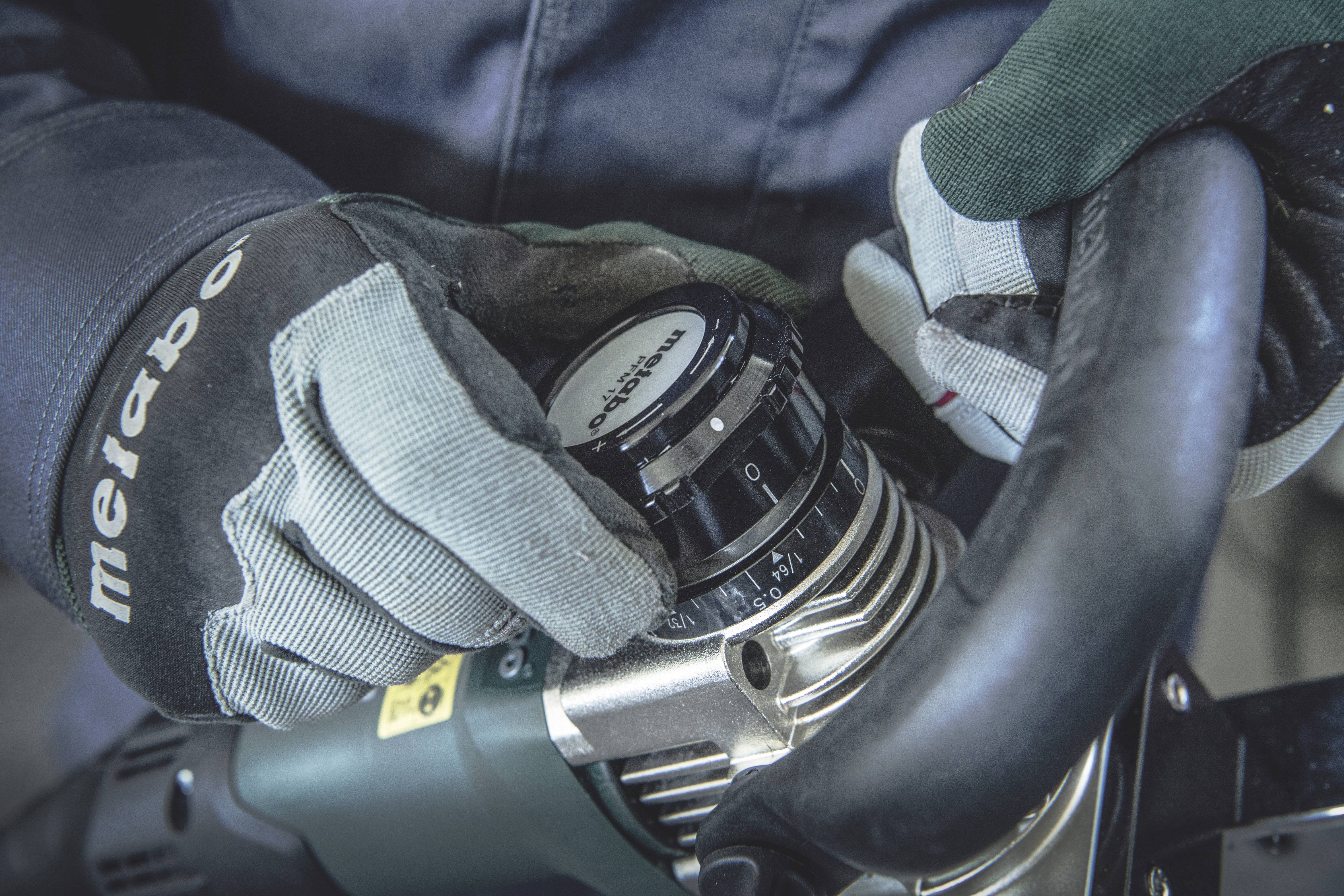 Osoba w rękawiczkach reguluje pokrętło na elektronarzędziu. Fokus skierowany jest na dłonie i pokrętło.