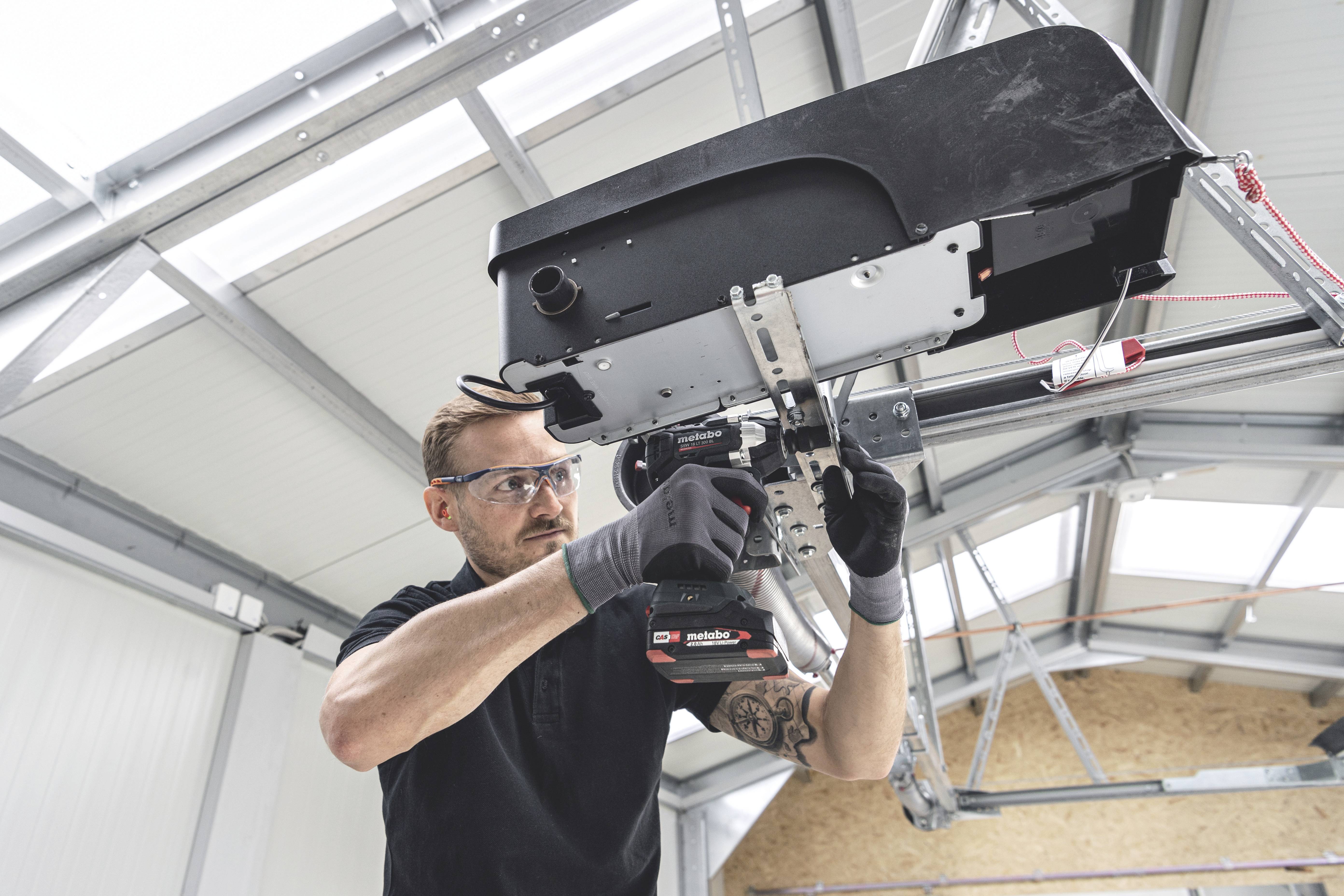 Mężczyzna przeprowadza montaż w nowoczesnym pomieszczeniu, pracując akumulatorowym wkrętakiem przy mechanicznym urządzeniu.