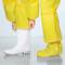 Osoba nosi żółty kombinezon ochronny i białe gumowce na szarym podłożu.