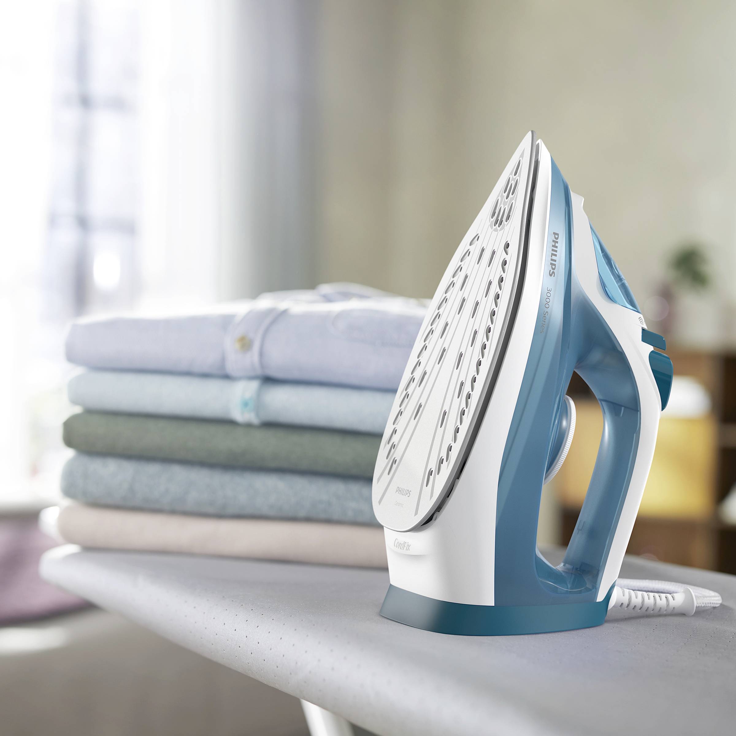 Żelazko obok ułożonych w stos, złożonych koszul na desce do prasowania.