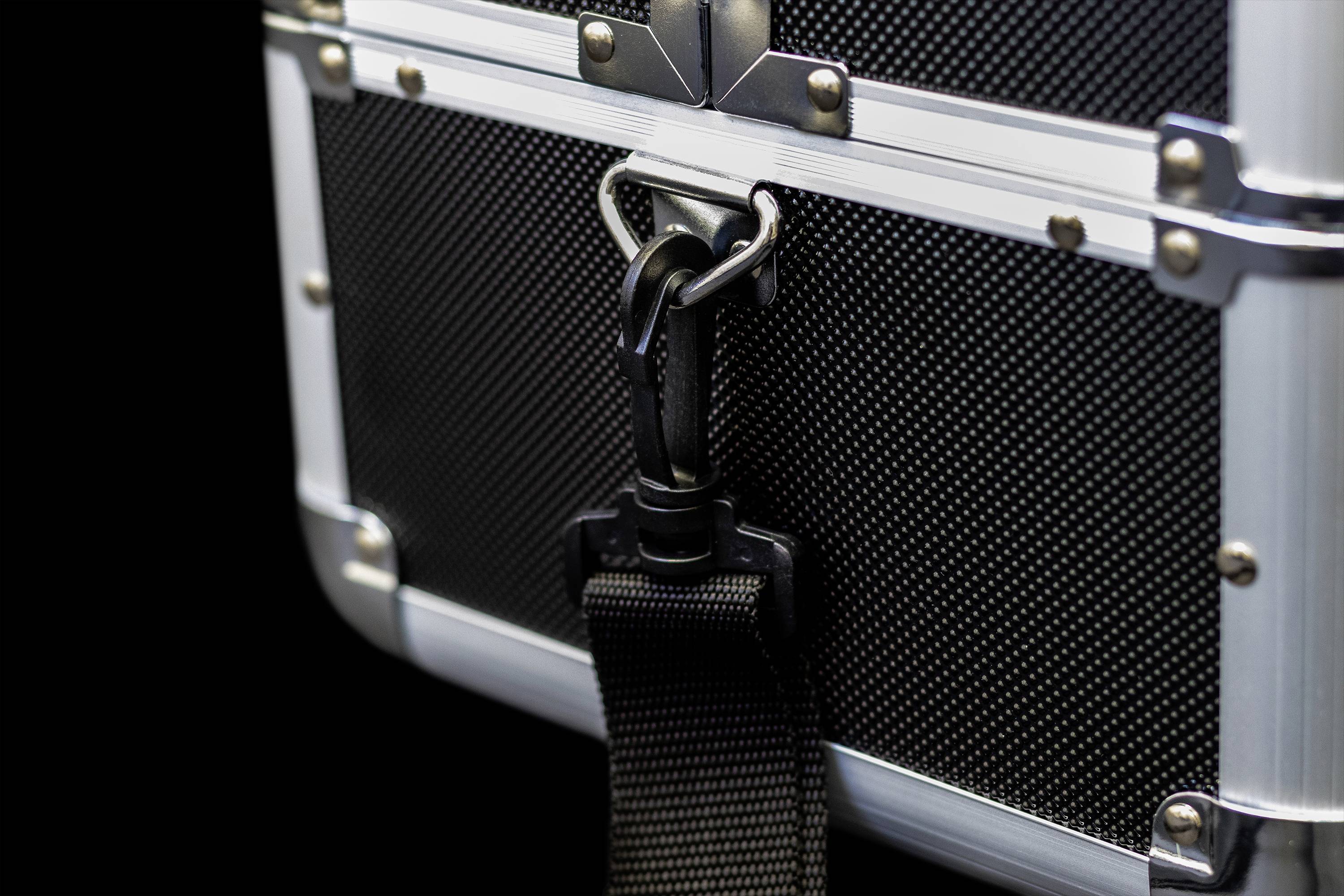 Zbliżenie czarnej walizki twardej z metalowymi klamrami i dużym karabińczykiem przymocowanym do paska.