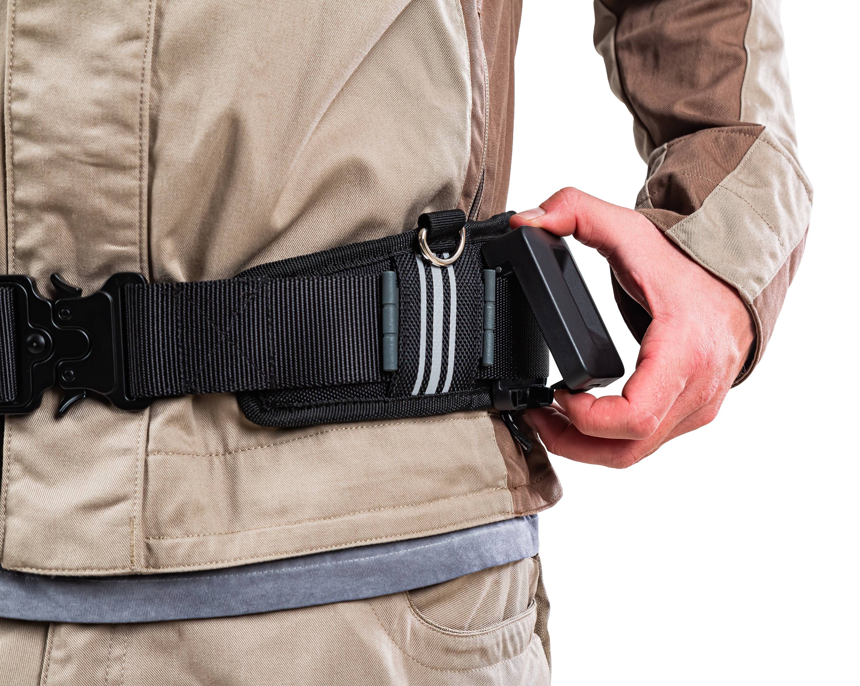 Osoba zakłada czarny pas z metalową klamrą. Ubranie jest beżowe, a tło białe.