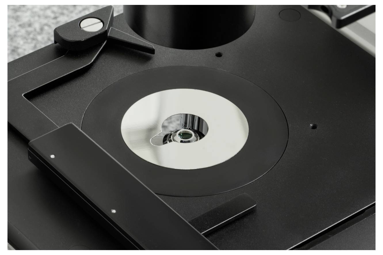 Mikroobiektyw nad okrągłą metaliczną powierzchnią, gotowy do badania lub analizy.