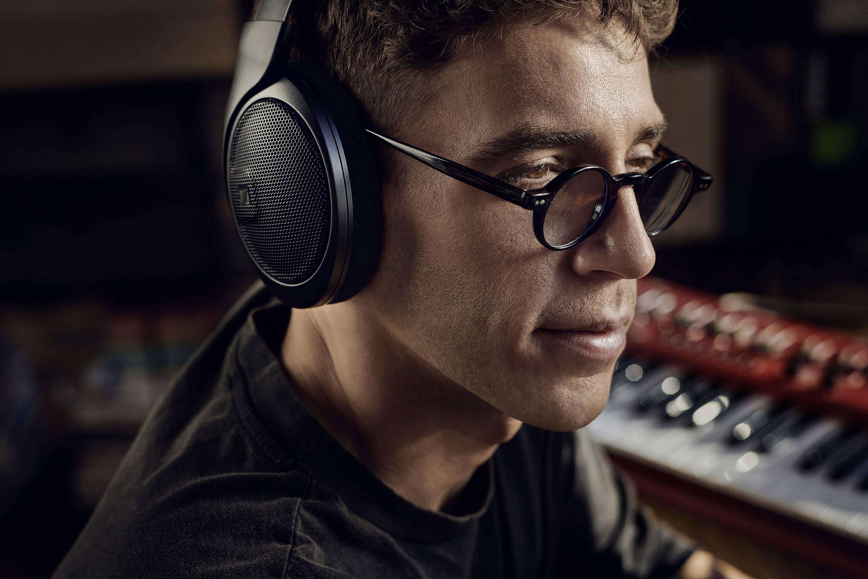 Mężczyzna w okularach i słuchawkach patrzy w skupieniu. W tle niewyraźnie widać klawiatury.