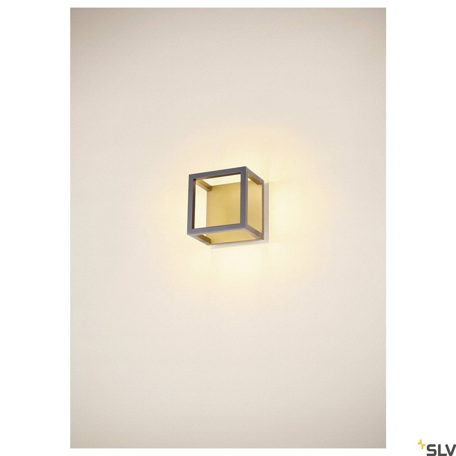 Kinkiet w kształcie sześcianu z ciepłym, delikatnym blaskiem świecącym na kremowej ścianie. Minimalistyczny design.