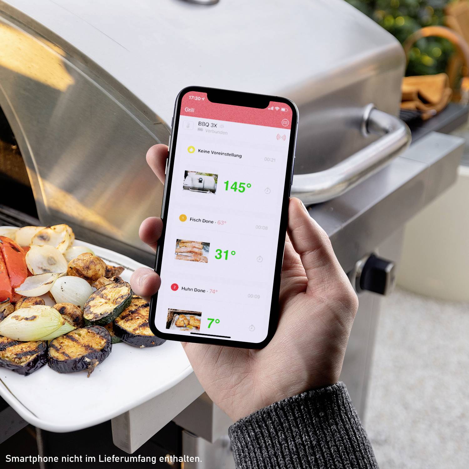 Osoba trzyma smartfon obok grilla: Aplikacja wyświetla trzy pomiary temperatury. Na pierwszym planie leżą grillowane warzywa.