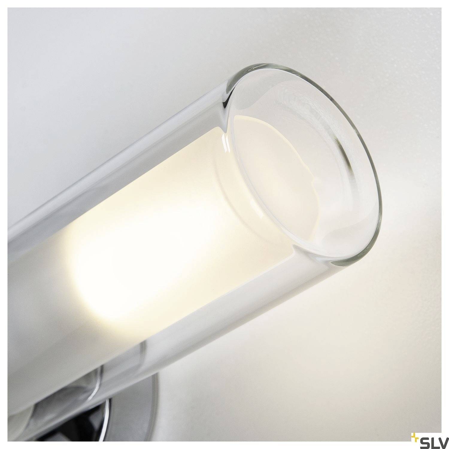 Nowoczesna, cylindryczna lampa ścienna z przezroczystego szkła, emitująca jasne światło, zamontowana na neutralnej ścianie.