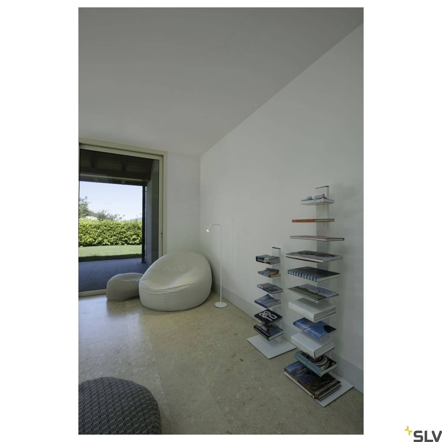 Jasny salon z fotelem tapicerowanym, lampą i nowoczesnymi regałami na książki. Panoramiczne okno z widokiem na ogród. Harmonijny, minimalistyczny design.
