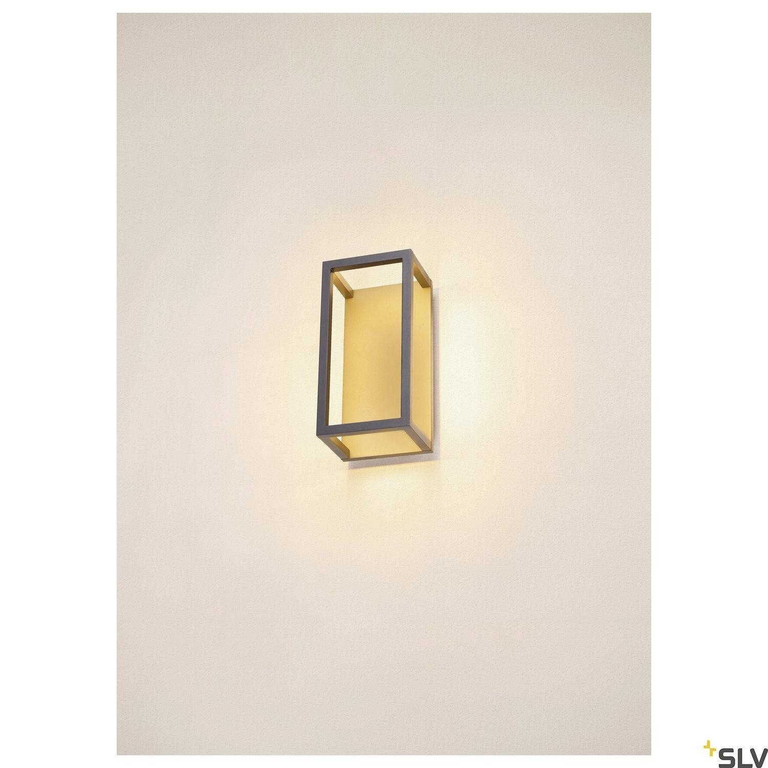 Prostokątna lampa ścienna z czarną ramą i ciepłym żółtym światłem, zamontowana na jasnej ścianie. Minimalistyczny design.
