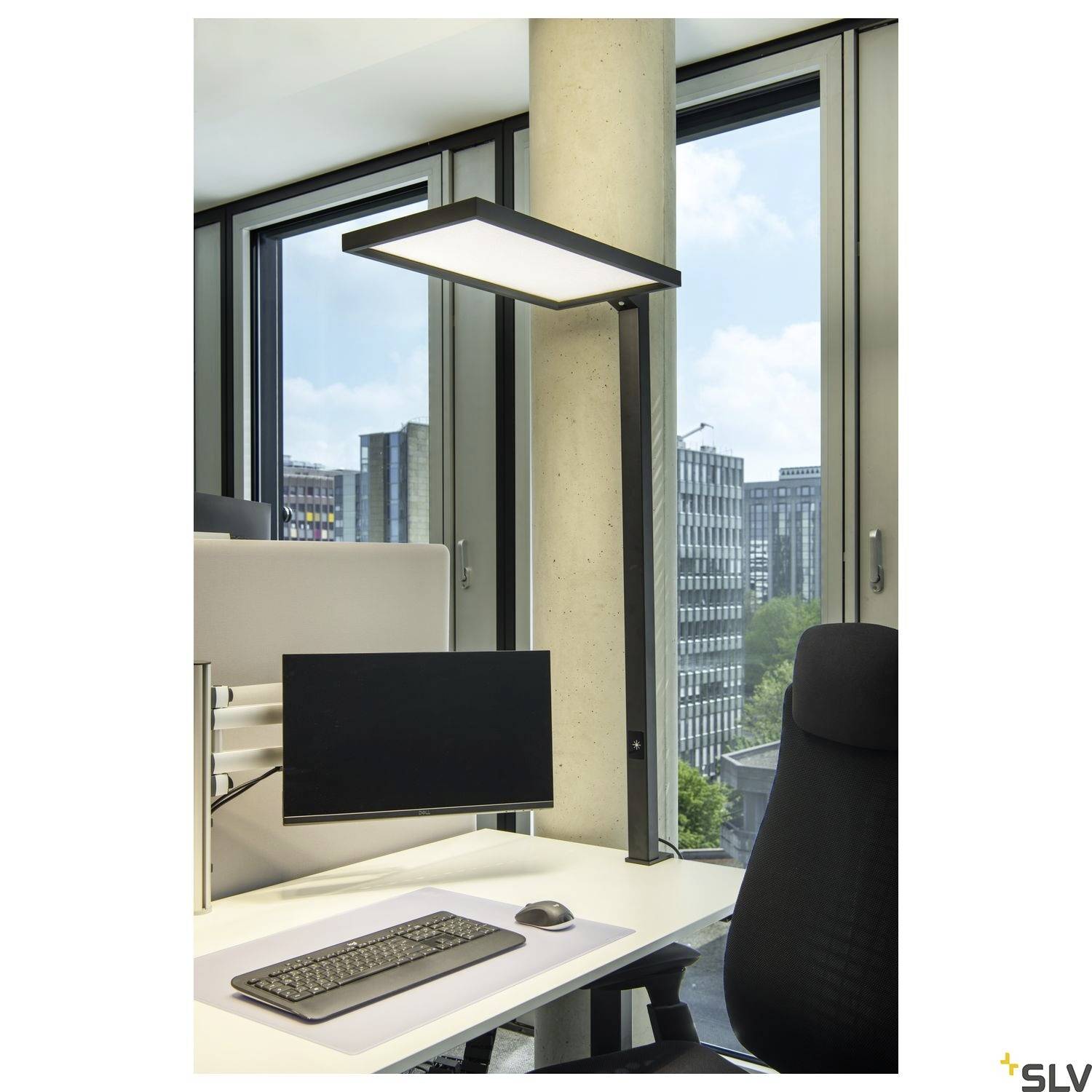 Biuro z nowoczesnym stanowiskiem pracy: monitor komputerowy, klawiatura i mysz na białym stole, duże okna w tle.