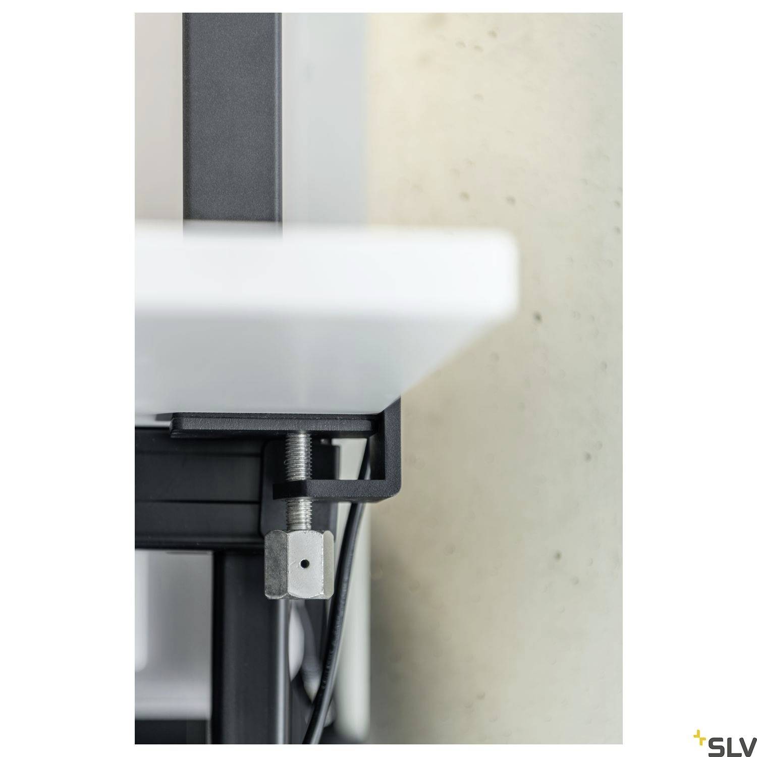 Zbliżenie metalowego zacisku przymocowanego do blatu stołu, prawdopodobnie będącego częścią systemu stołu z regulacją wysokości.