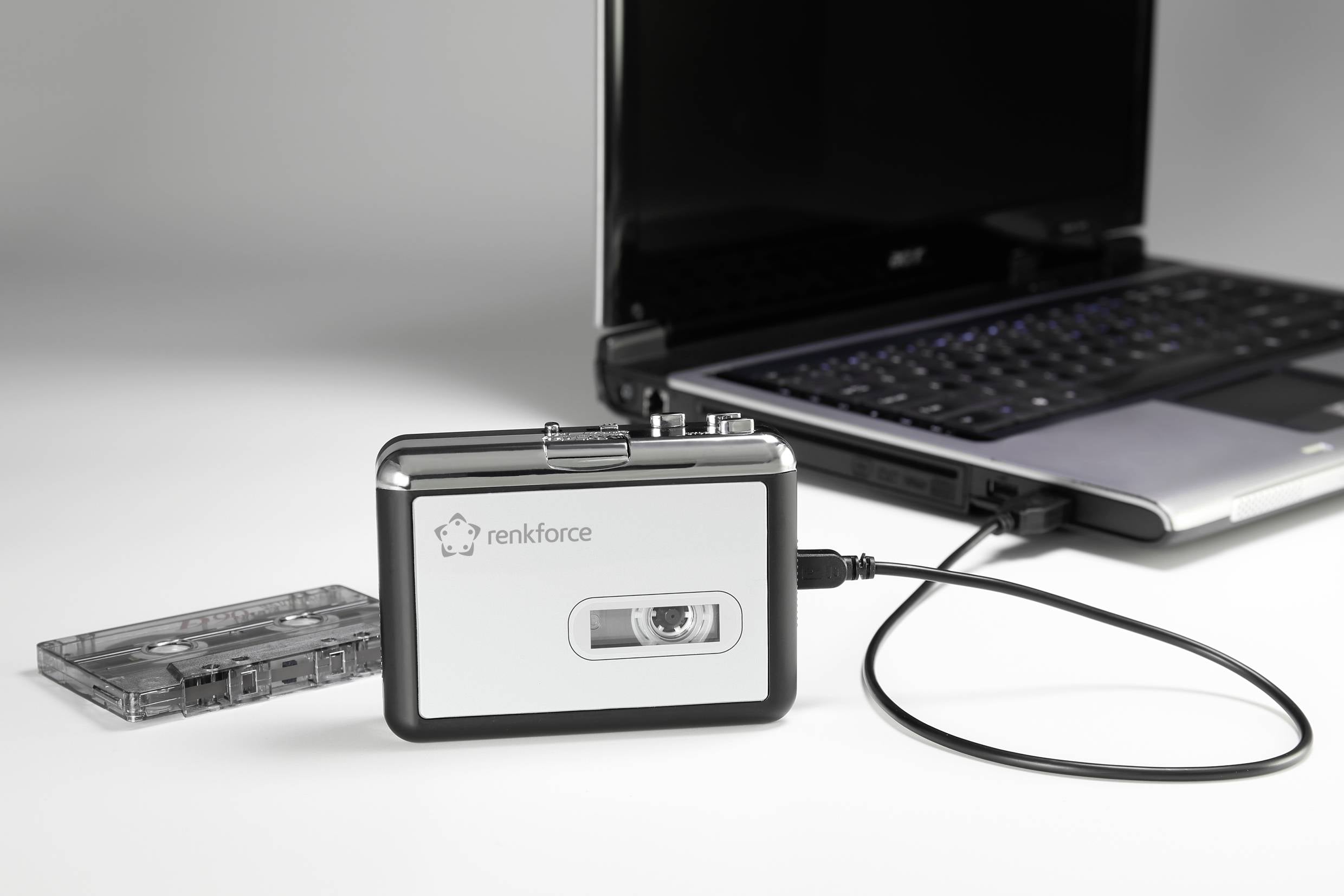 Odtwarzacz kasetowy firmy 'renkforce' podłączony do laptopa. Obok leży kaseta. Laptop jest włączony.