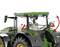 Traktor z zielonym dachem i dużymi kołami, czerwone strzałki wskazują na ruchomą część z tyłu kabiny kierowcy.