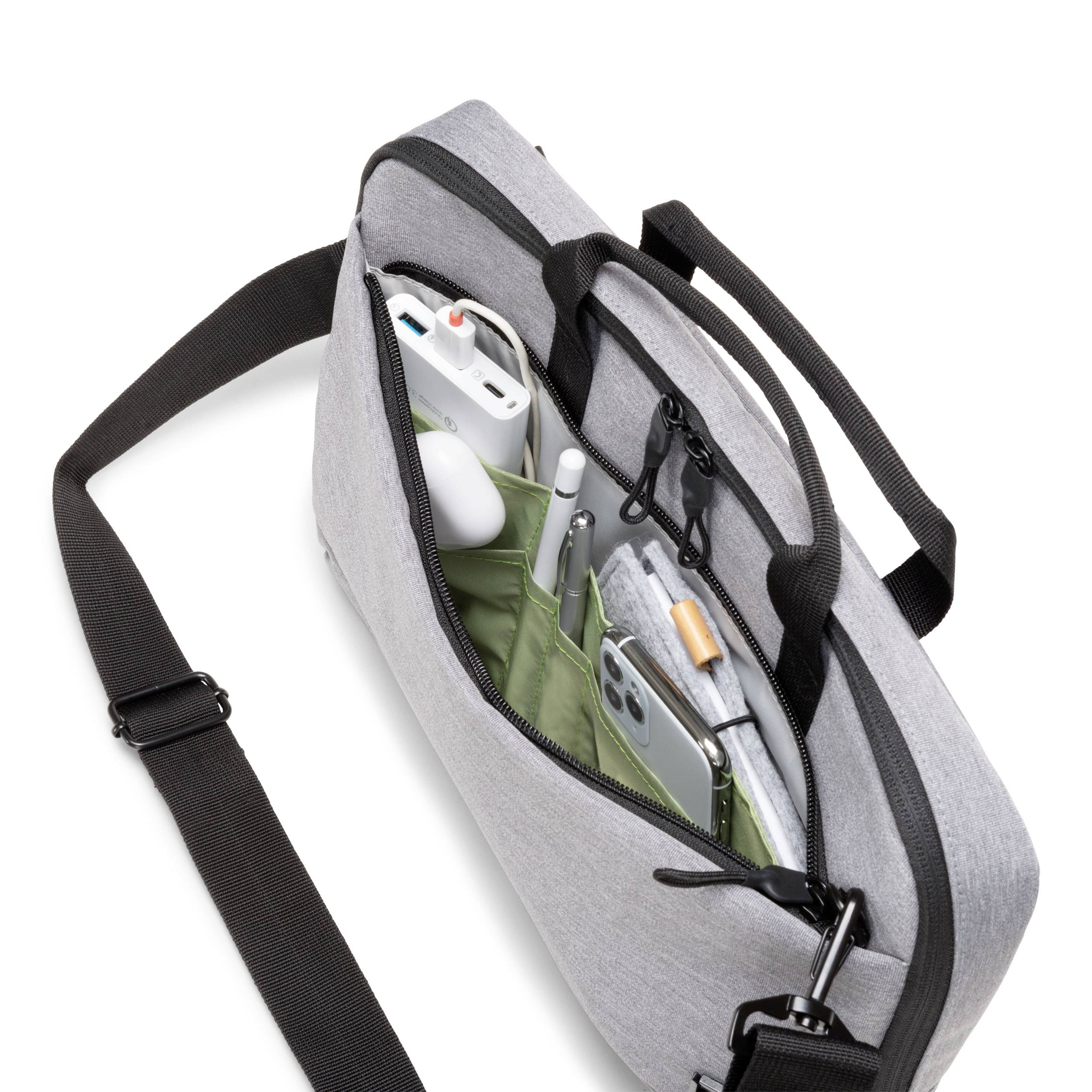 Szara torba na ramię z otwartą kieszenią na zamek błyskawiczny, widoczne są smartfon, słuchawki, ładowarka i długopis.
