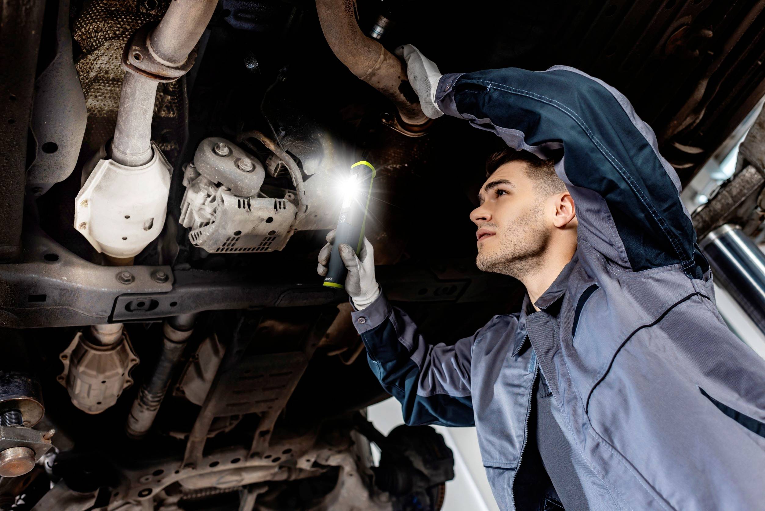 Mechanik sprawdza podwozie samochodu latarką w warsztacie.
