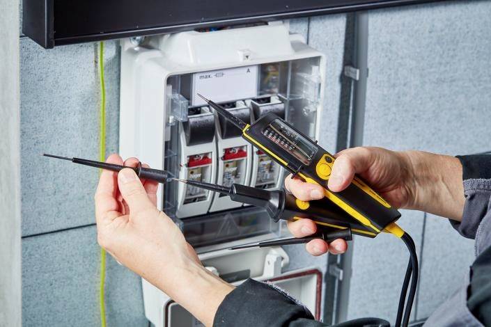 Osoba używa miernika elektrycznego do sprawdzania połączeń elektrycznych w szafce sterowniczej.