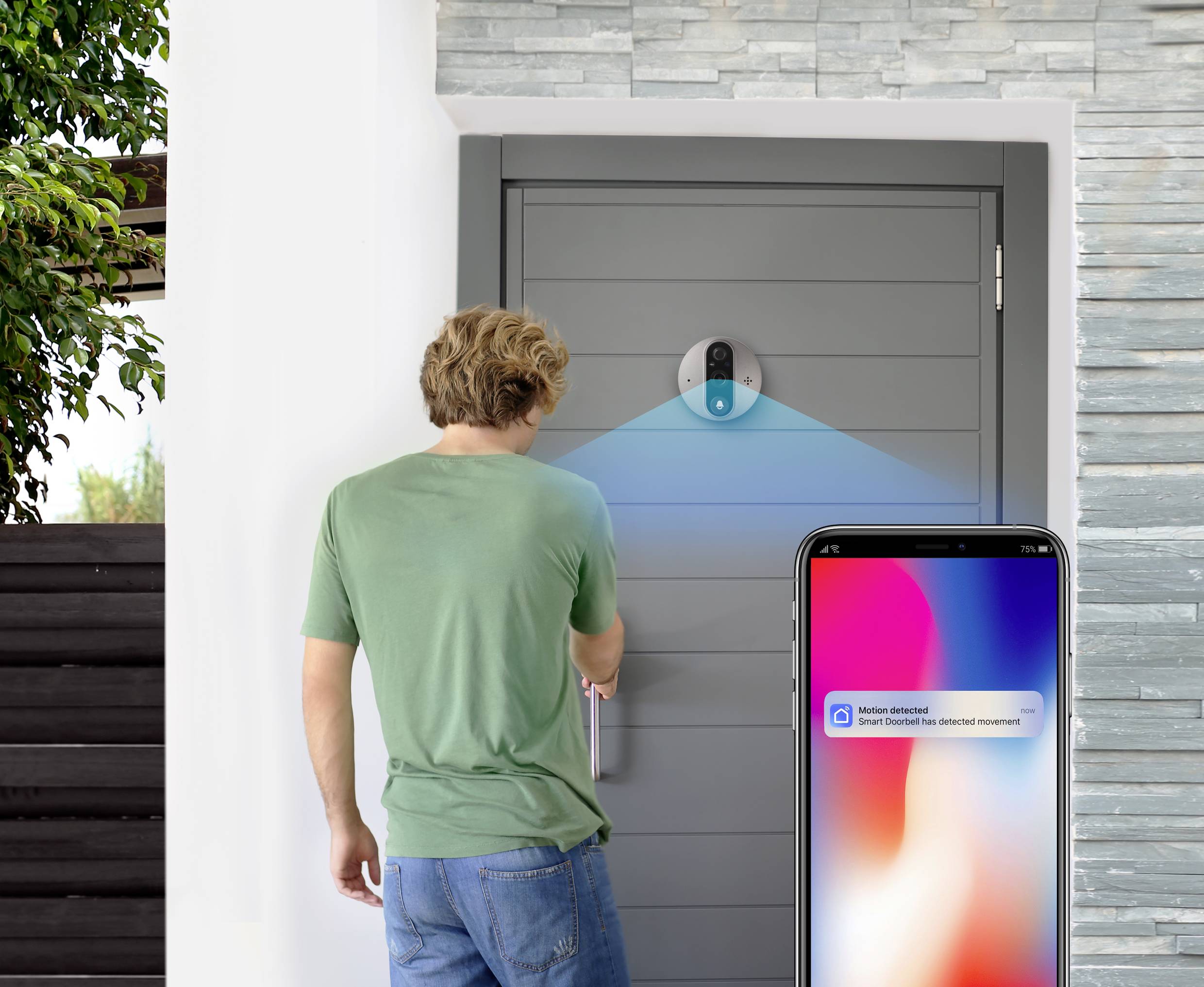 Mężczyzna otwiera drzwi za pomocą zamka sterowanego smartfonem. Powiadomienie na telefonie wyświetla komunikat 'Wykryto ruch'.