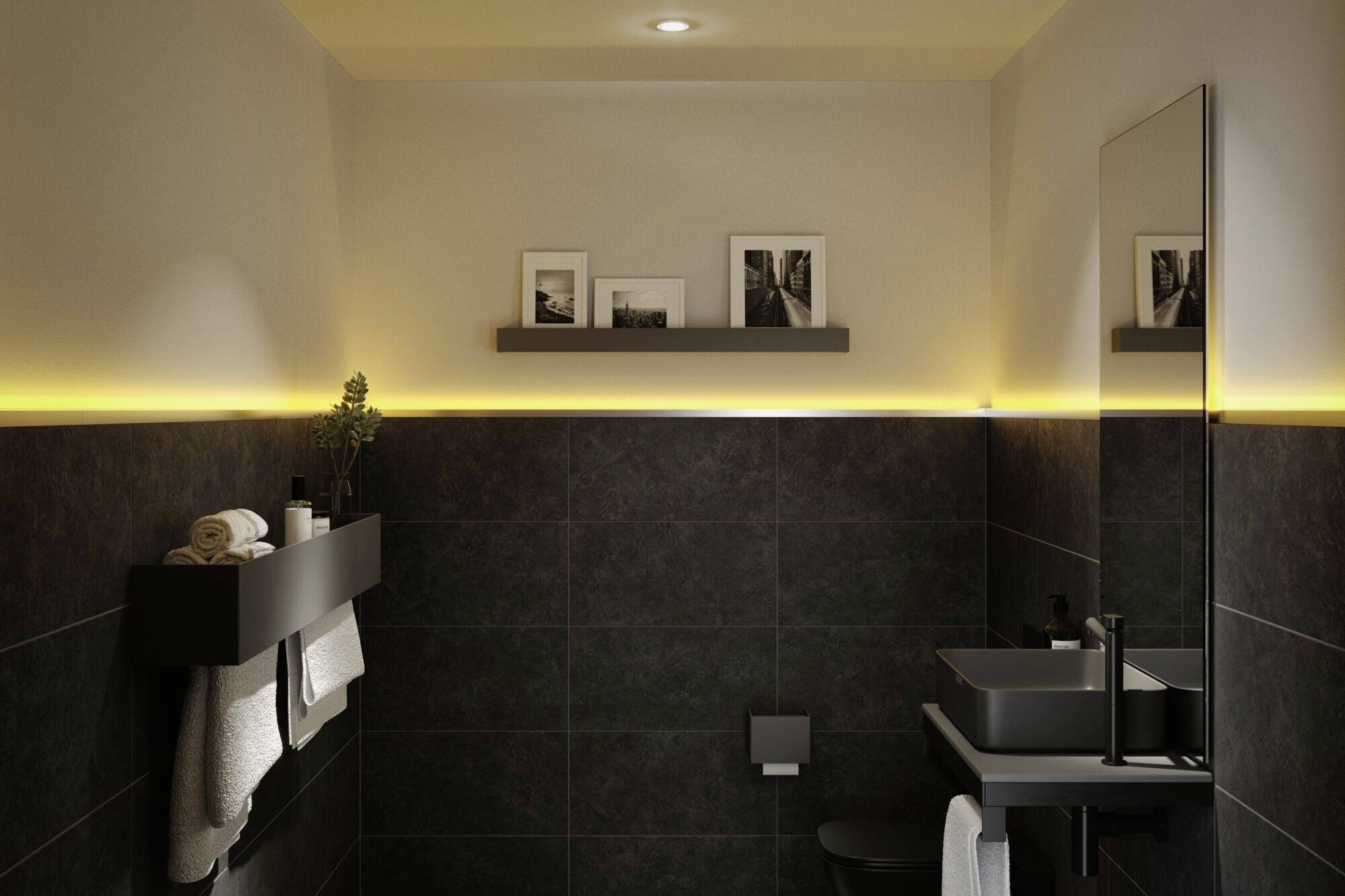 Nowoczesna łazienka z ciemnymi płytkami i ciepłym, pośrednim oświetleniem. Na ścianie wiszą oprawione obrazy i lustro.