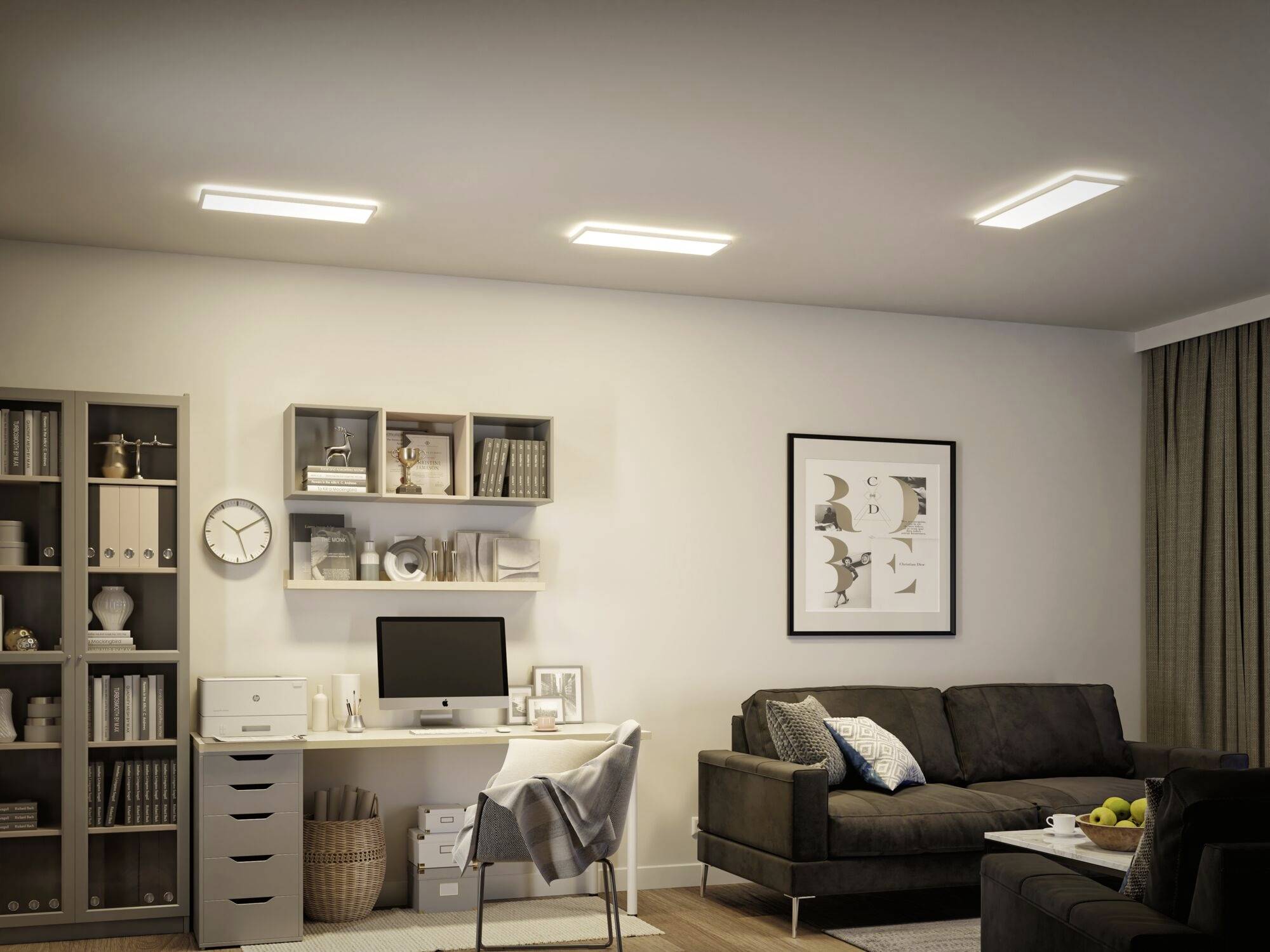 Salon z biurkiem, regałem i sofą. Monitor komputerowy i dekoracje na biurku, regały pełne książek.