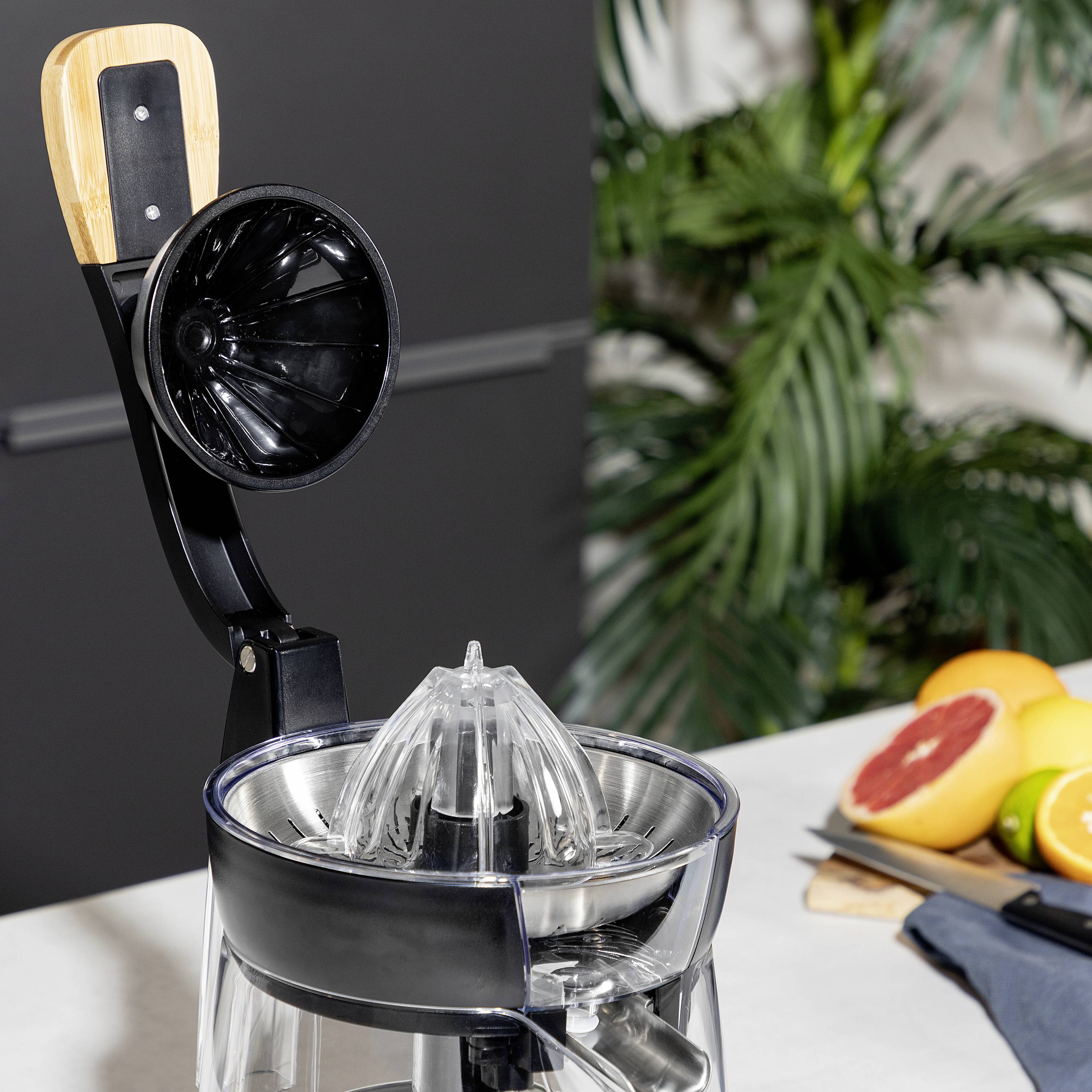 Na blacie kuchennym stoi wyciskacz do cytrusów. Obok leżą pocięte owoce cytrusowe na desce do krojenia.