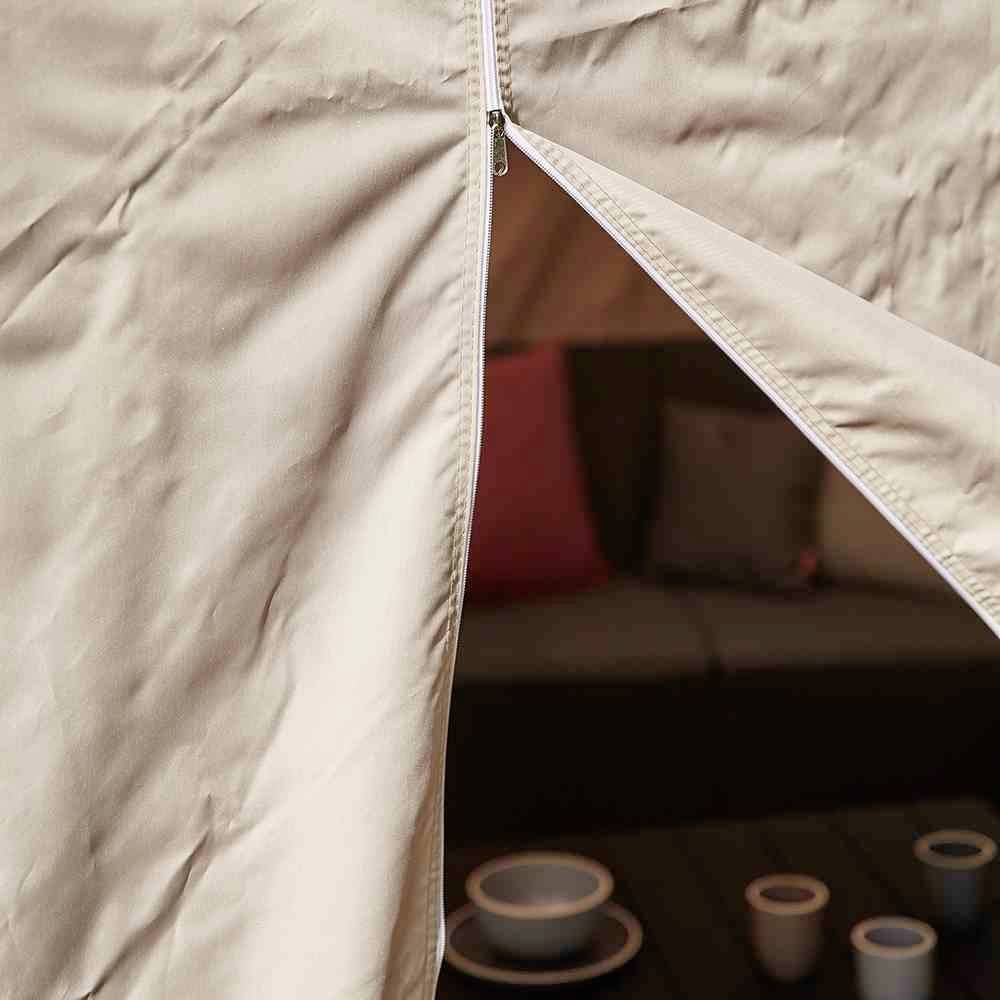 Jasnobrązowy namiot jest częściowo otwarty, a w jego wnętrzu widać kanapę z poduszkami oraz mały stolik z zastawą stołową.