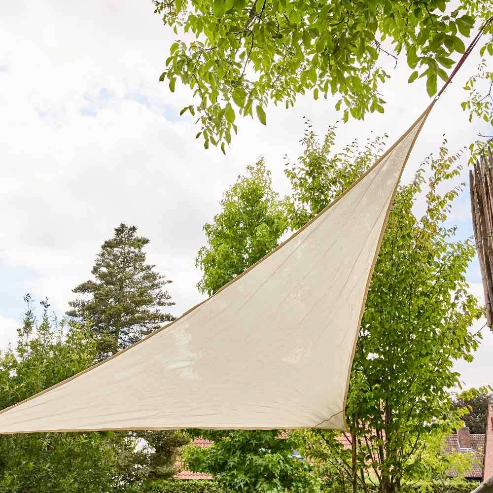 Żagiel przeciwsłoneczny w ogrodzie, otoczony zielonymi drzewami i błękitnym niebem, zapewnia cień w słoneczny dzień.